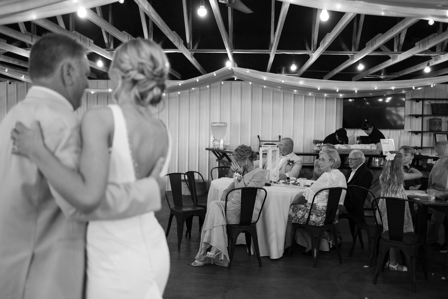 Wedding reception dance floor with couples dancing in formal attire under decorative draping and lighting.