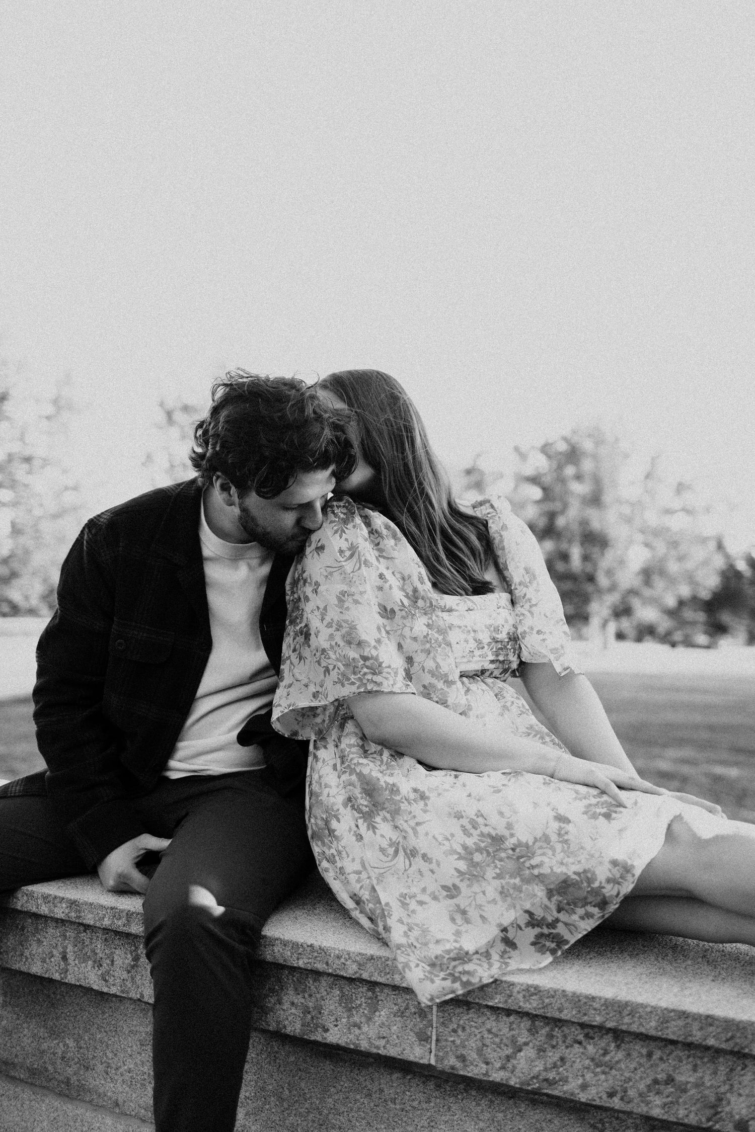 A black and white photo of a couple sitting close together on stone steps outdoors.