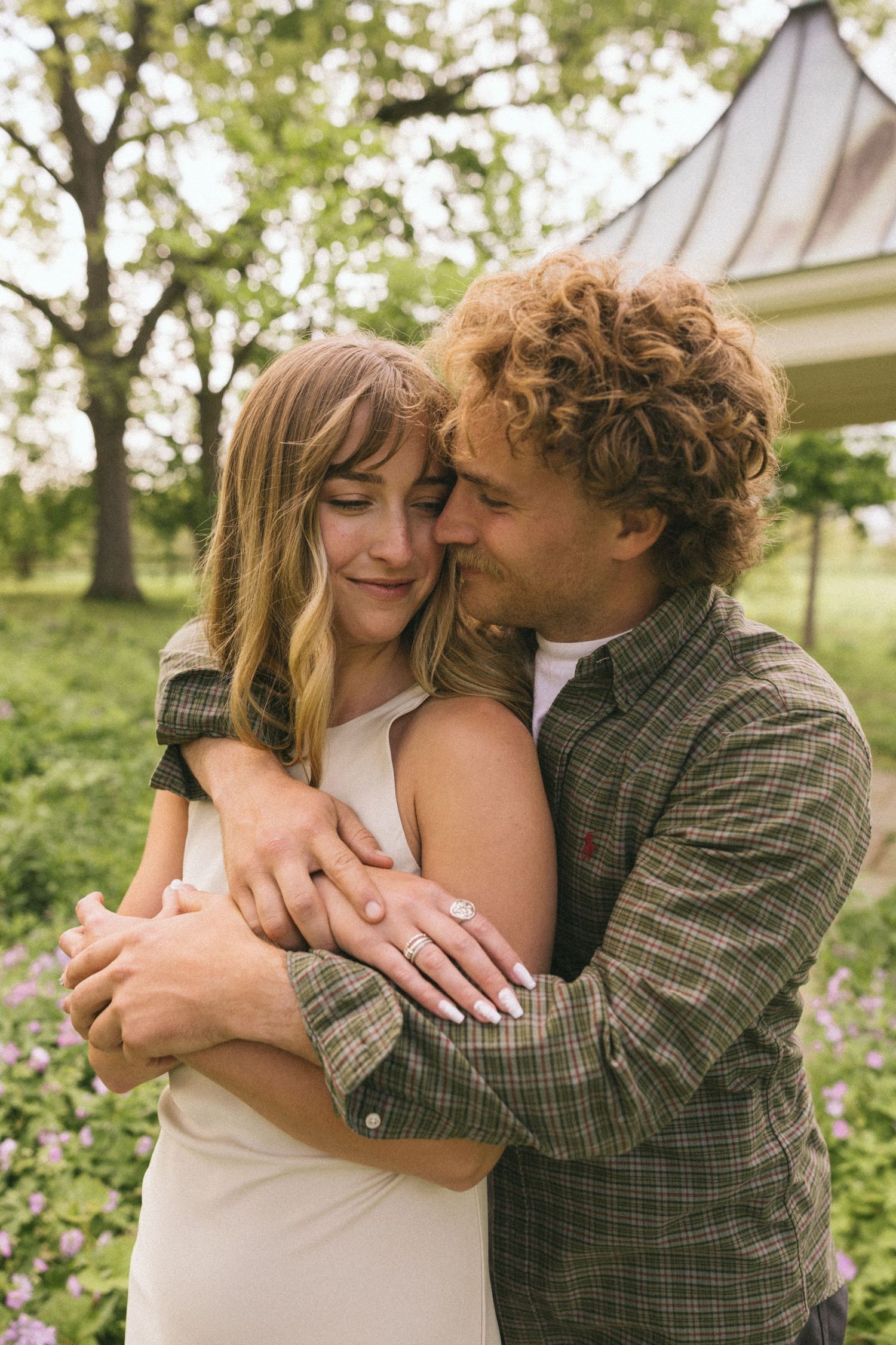 A couple shares an intimate embrace in a garden setting with spring trees in the background.