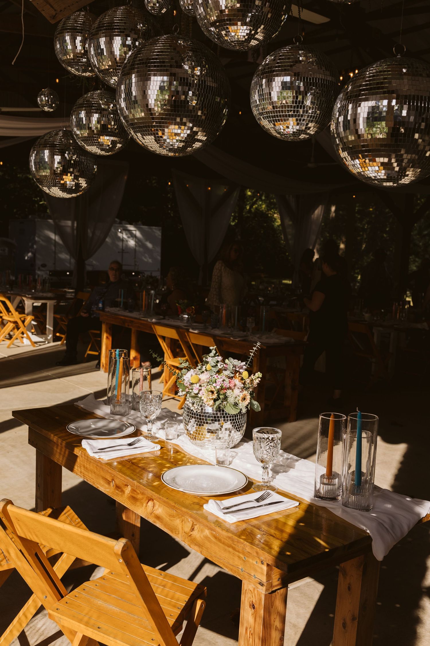 Elegant reception tables with disco balls overhead and wooden chairs in a dimly lit venue.