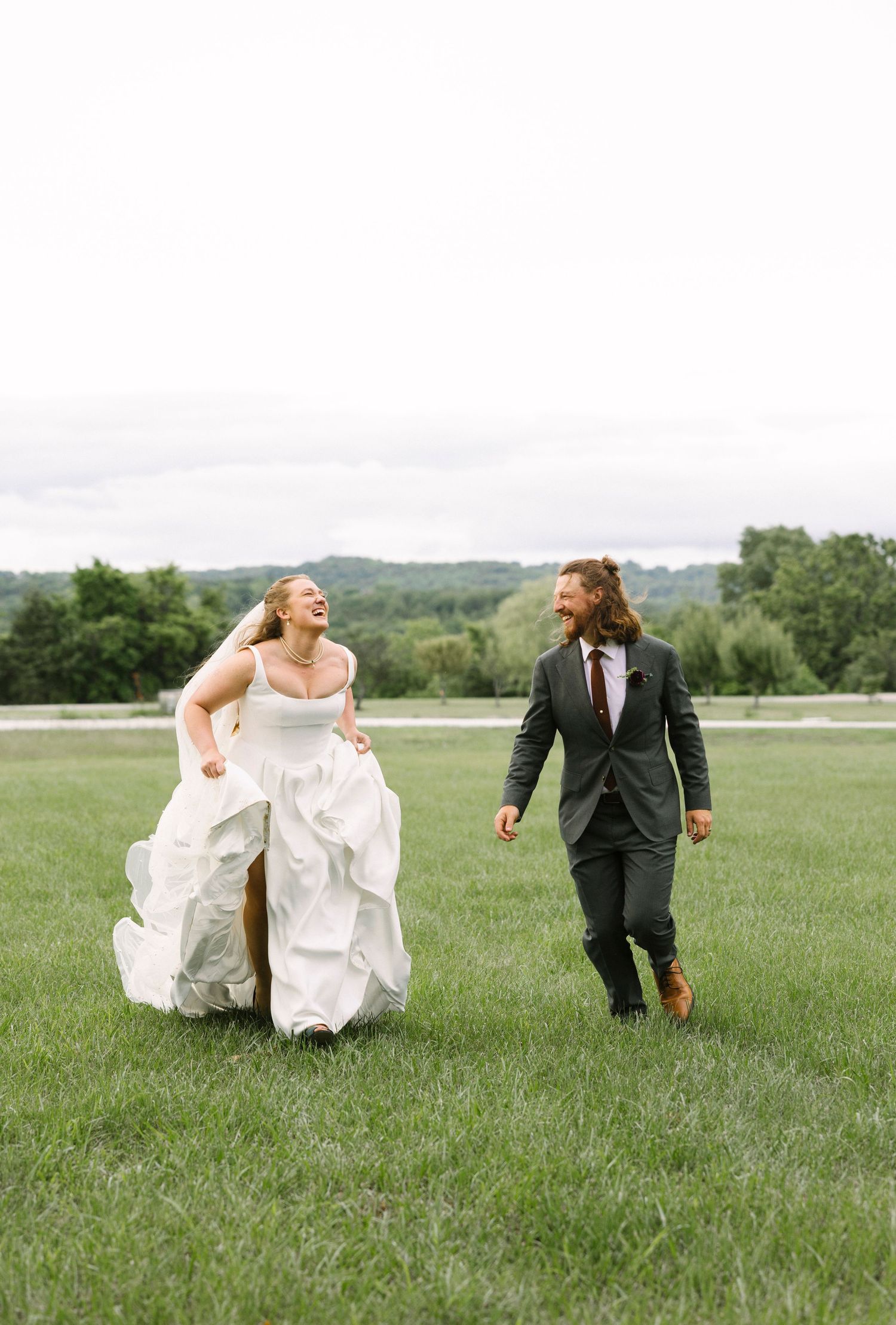 A candid shot of newlyweds walking and laughing together in a scenic meadow.