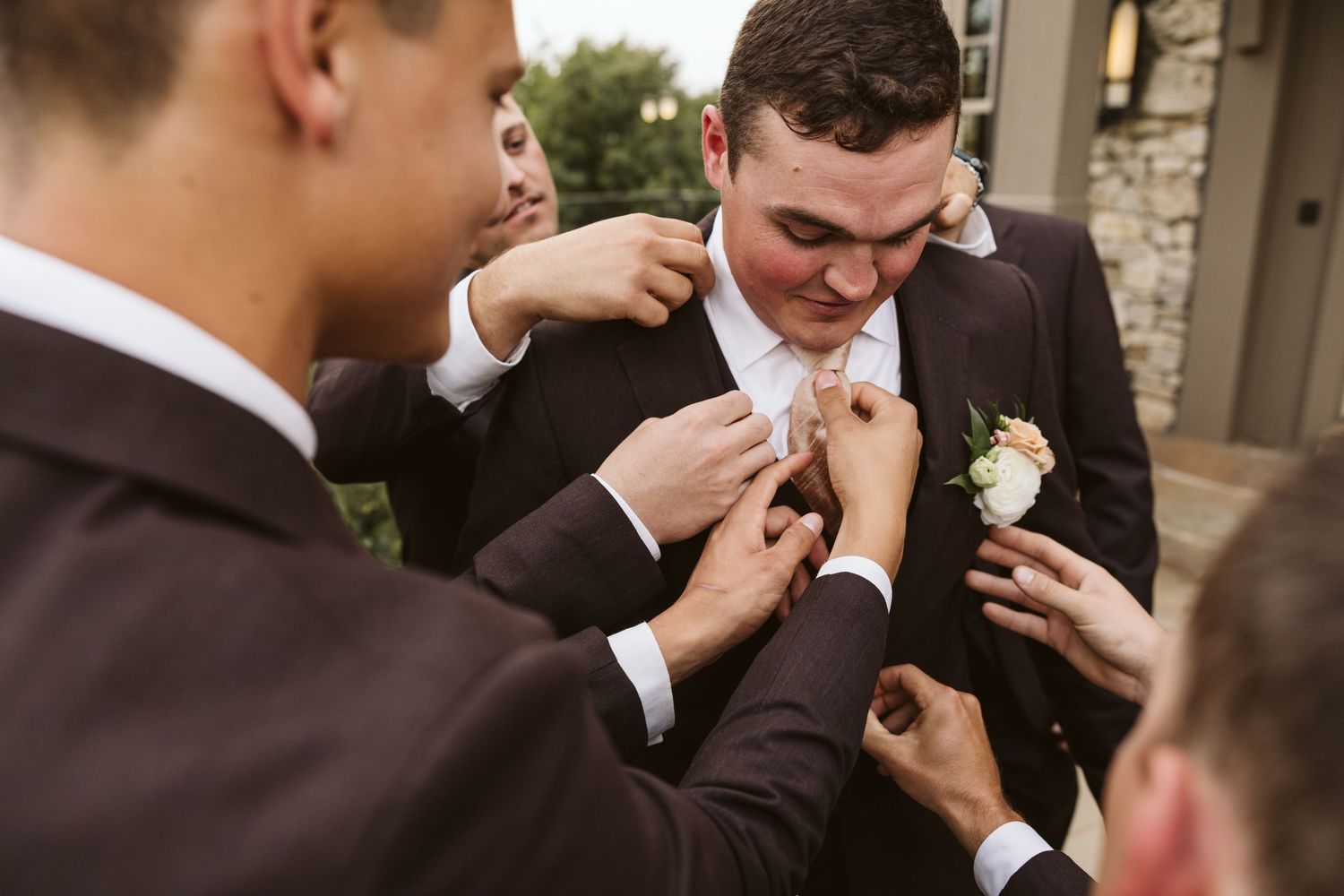 Groomsmen helping adjust the groom's boutonniere before the wedding ceremony.
