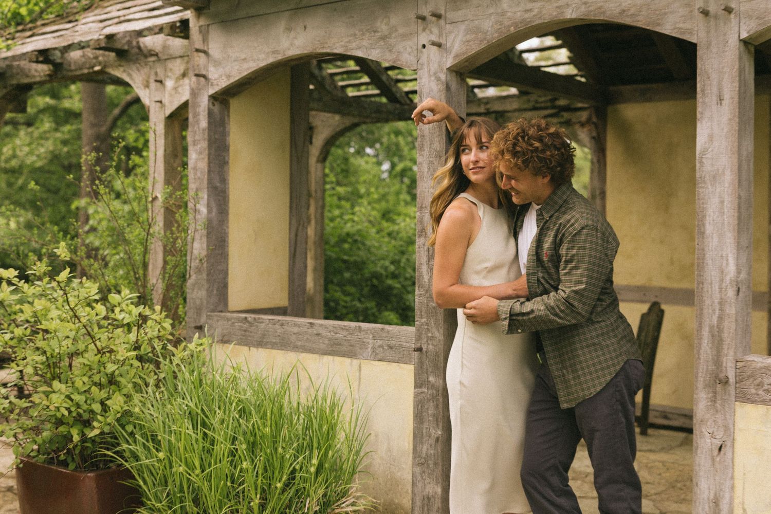 A romantic moment shared under a covered garden pergola with stone floors and greenery.