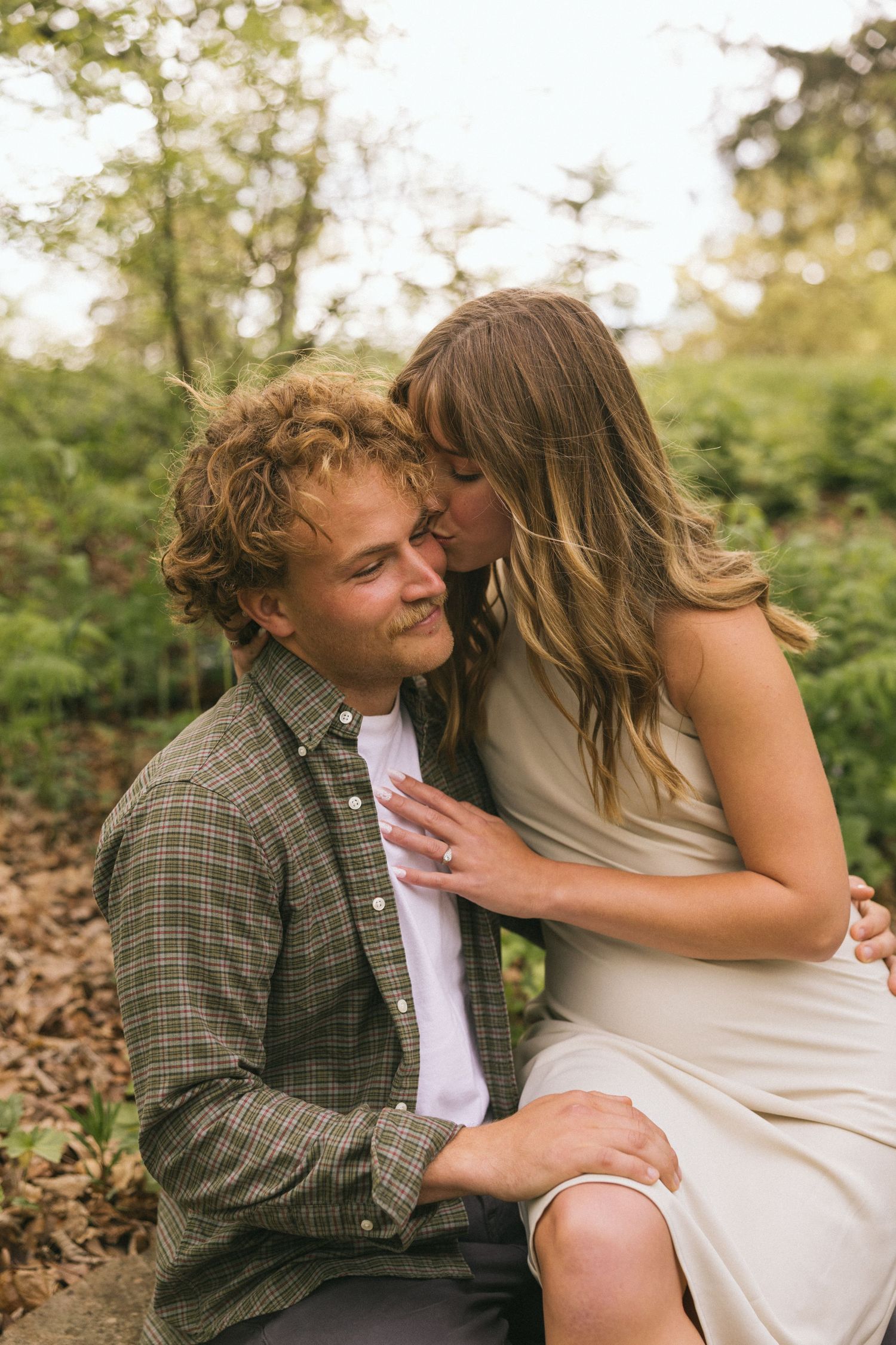 A couple shares an intimate moment sitting together outdoors in autumn surrounded by fallen leaves.