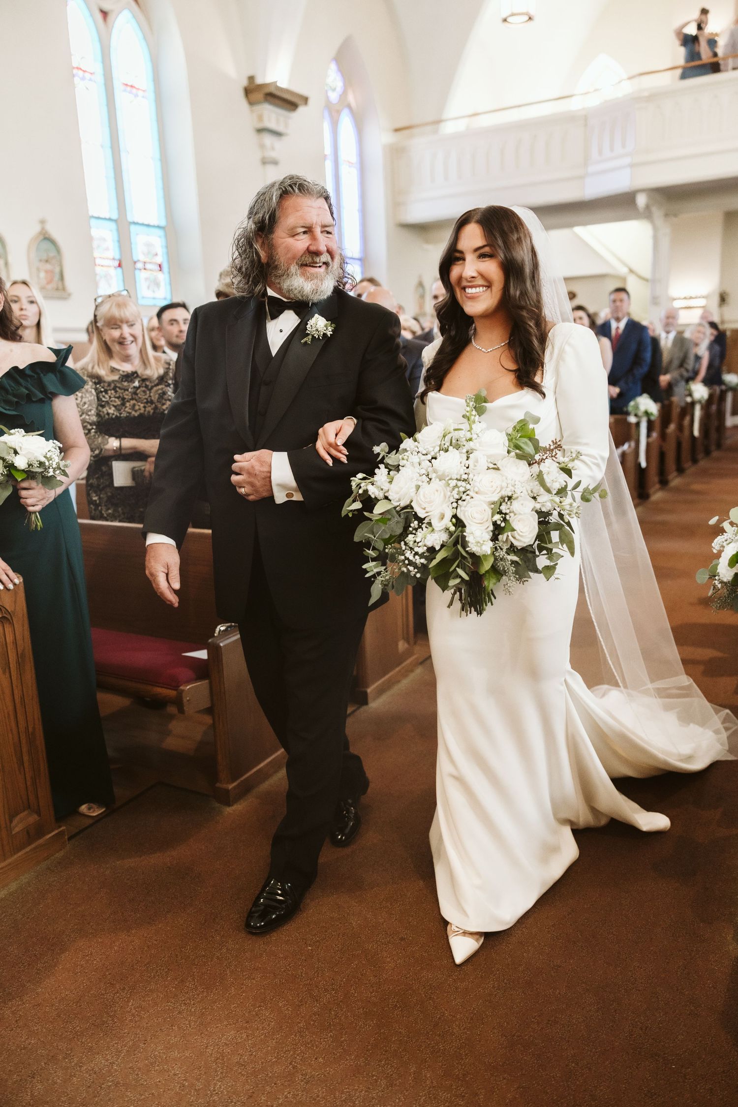 Wedding couple walking down church aisle decorated with white floral arrangements.