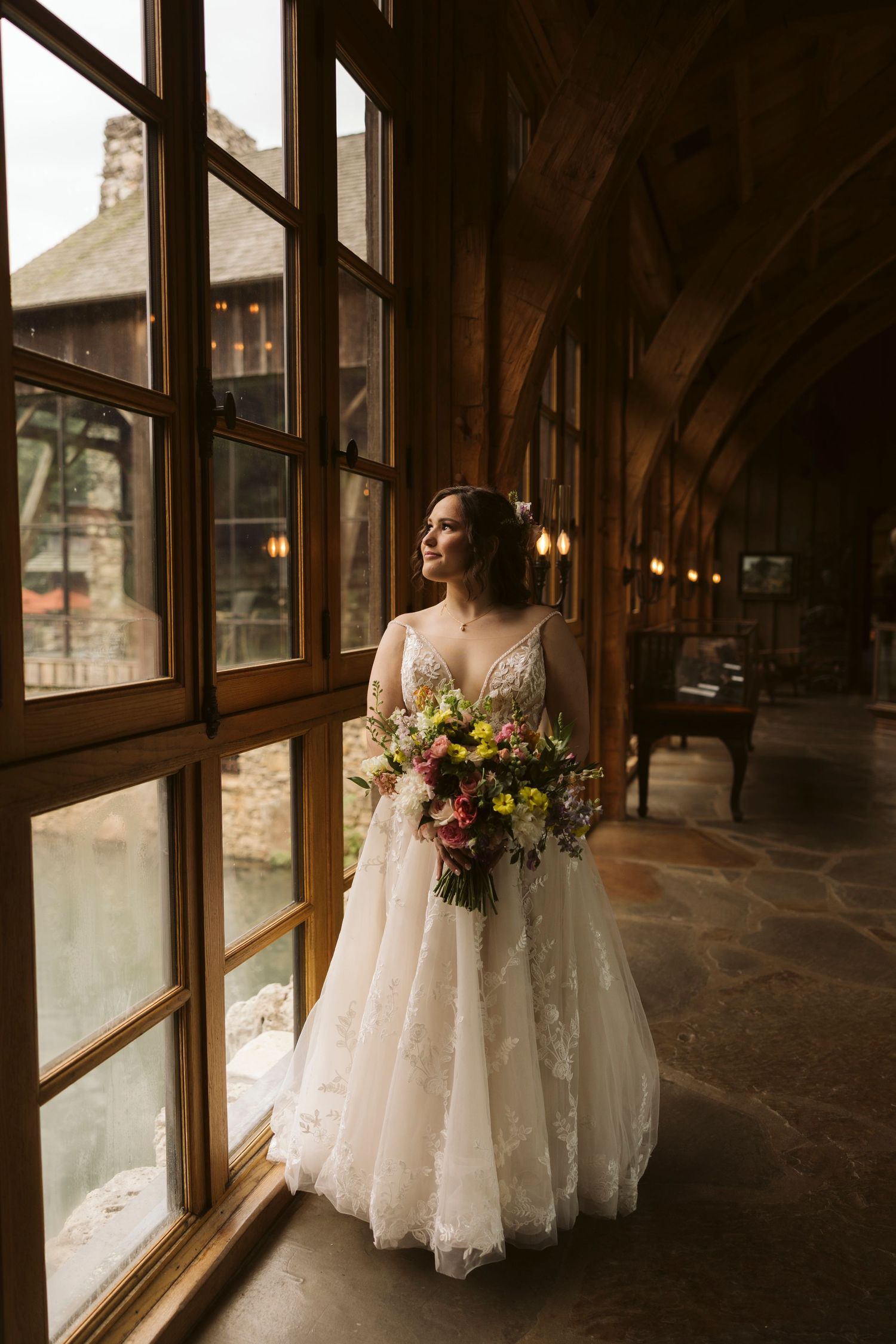 A wedding dress is beautifully displayed in a rustic indoor setting with wooden beams and natural lighting.