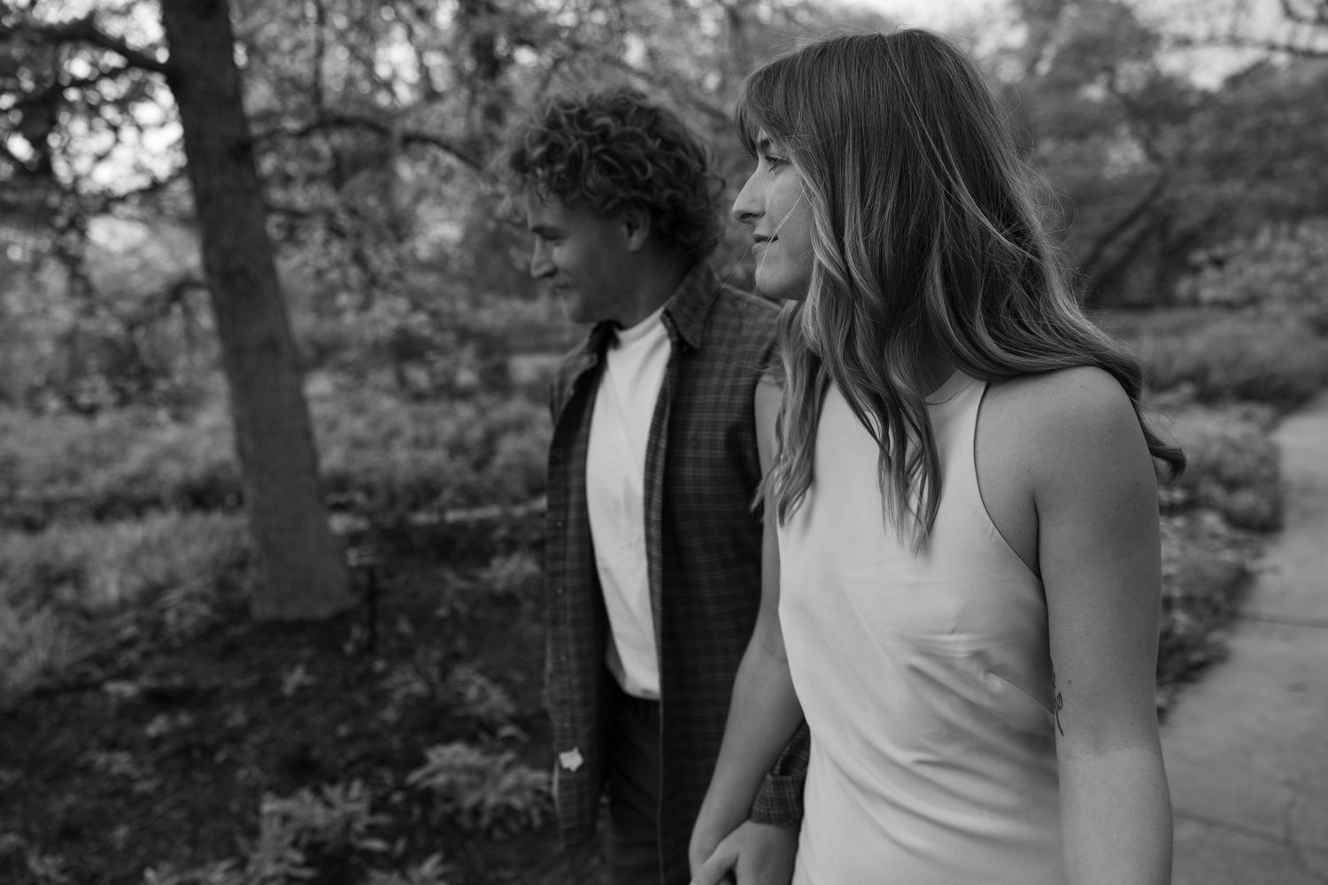 A black and white portrait of a couple in casual attire standing together outdoors.