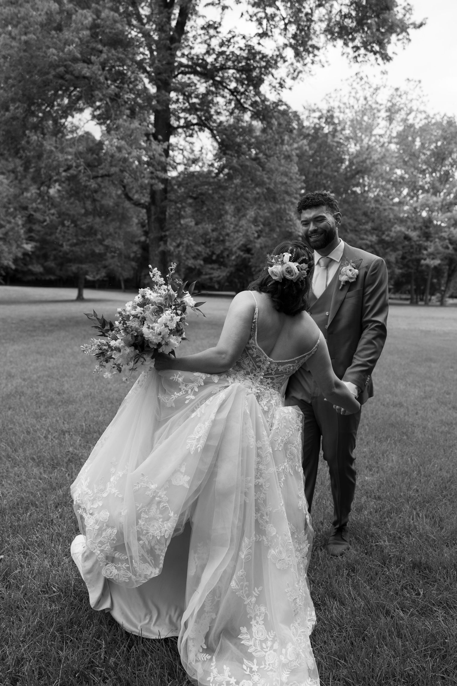 Couple walks through a grassy field with the bride's lace dress flowing in the wind.