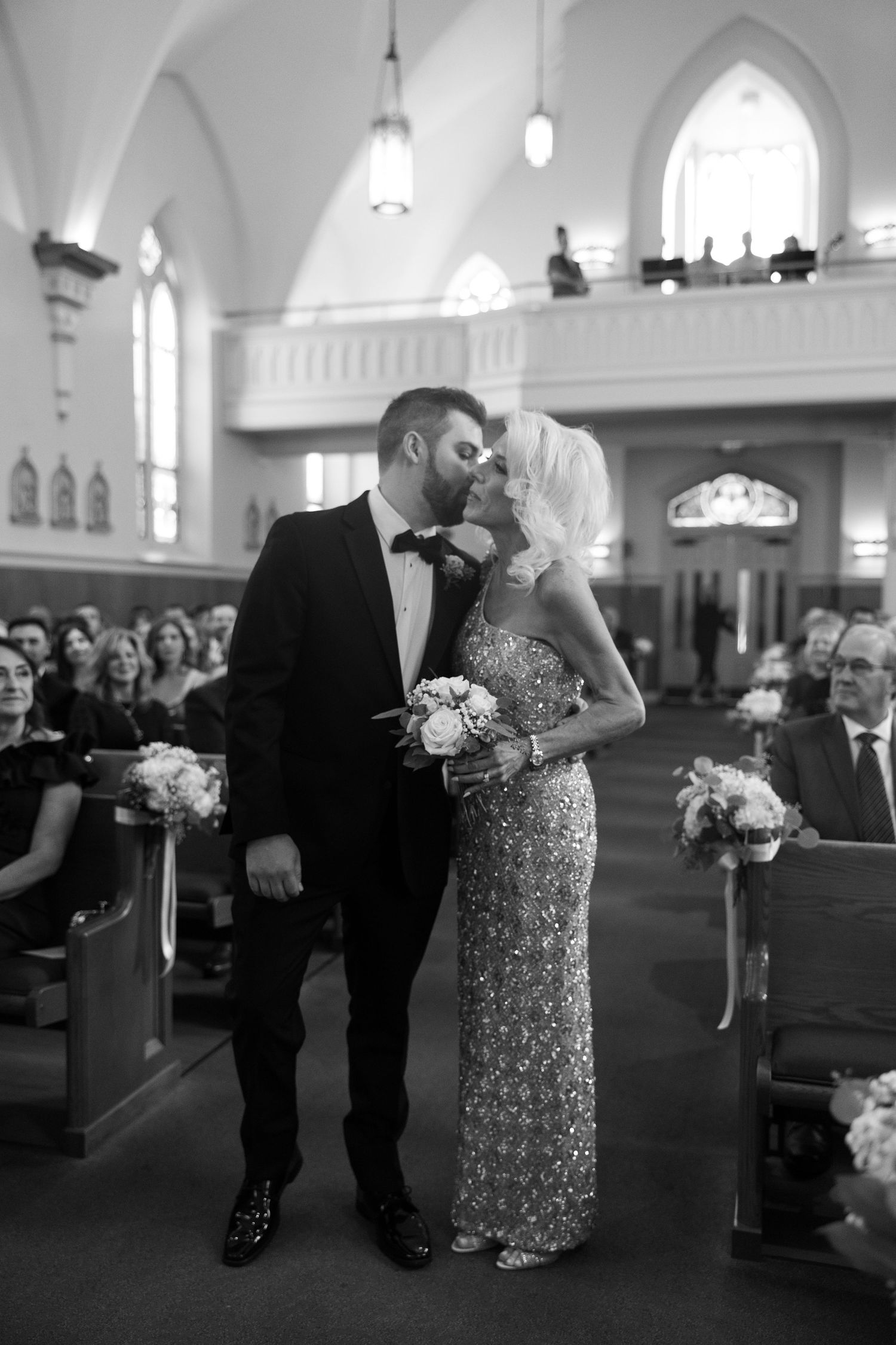 Wedding moment in a church with sparkling dress and decorative floral arrangements.