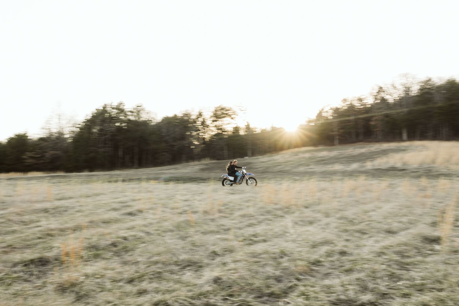 A distant silhouette of someone riding a dirt bike across a sunlit field.