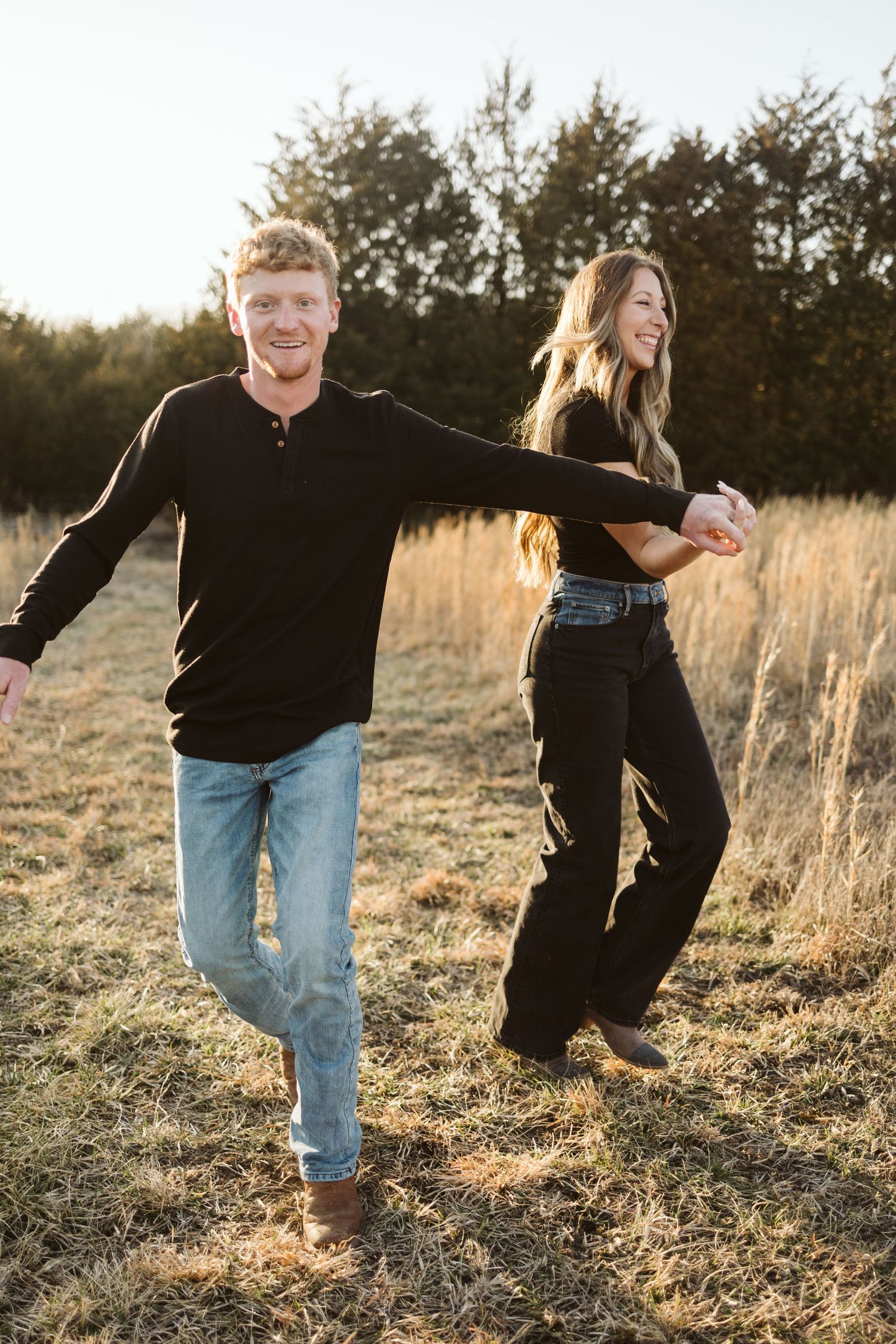 Playful couple dancing in tall grass field during golden hour.