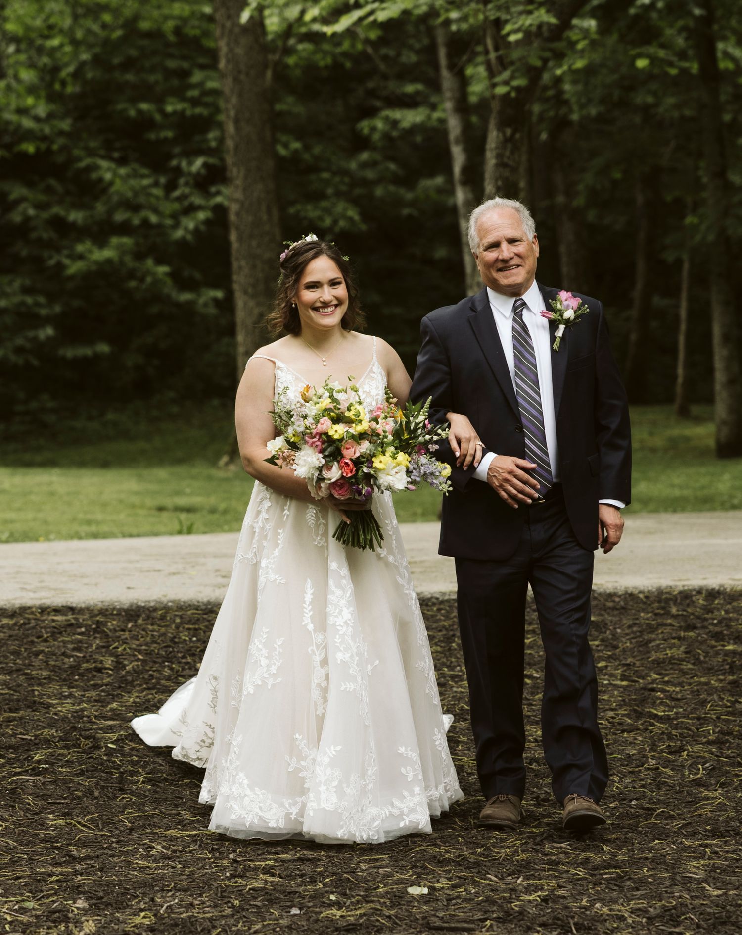 A wedding procession walks along a natural outdoor path during the celebration.