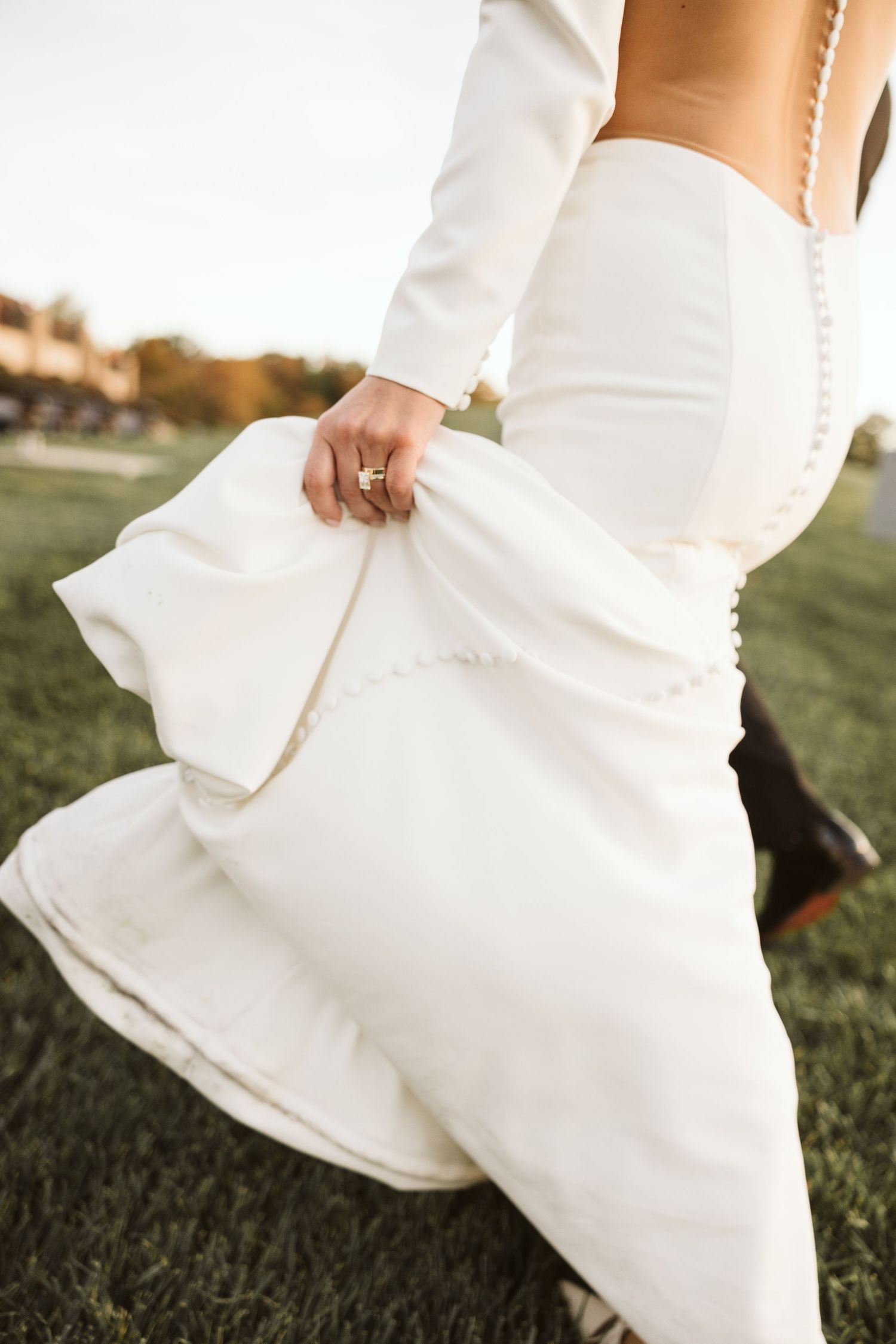 Close-up details of a flowing white wedding dress against green grass.