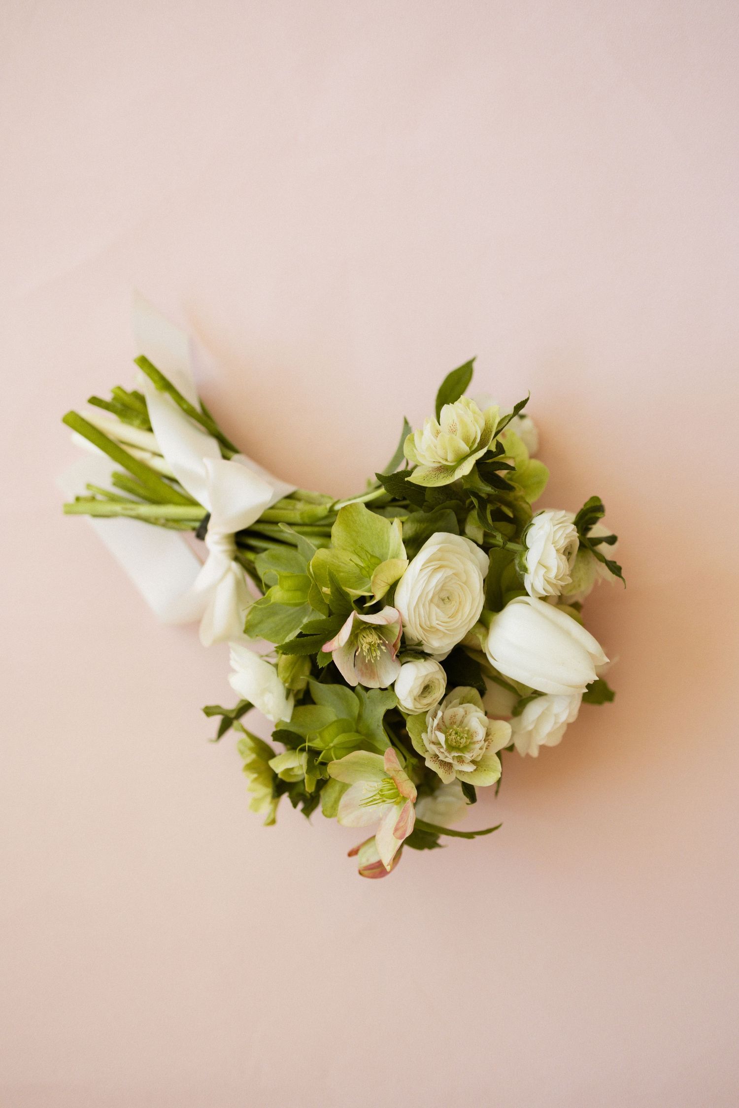 Delicate white roses and green foliage arranged in an elegant bouquet against a soft pink background.