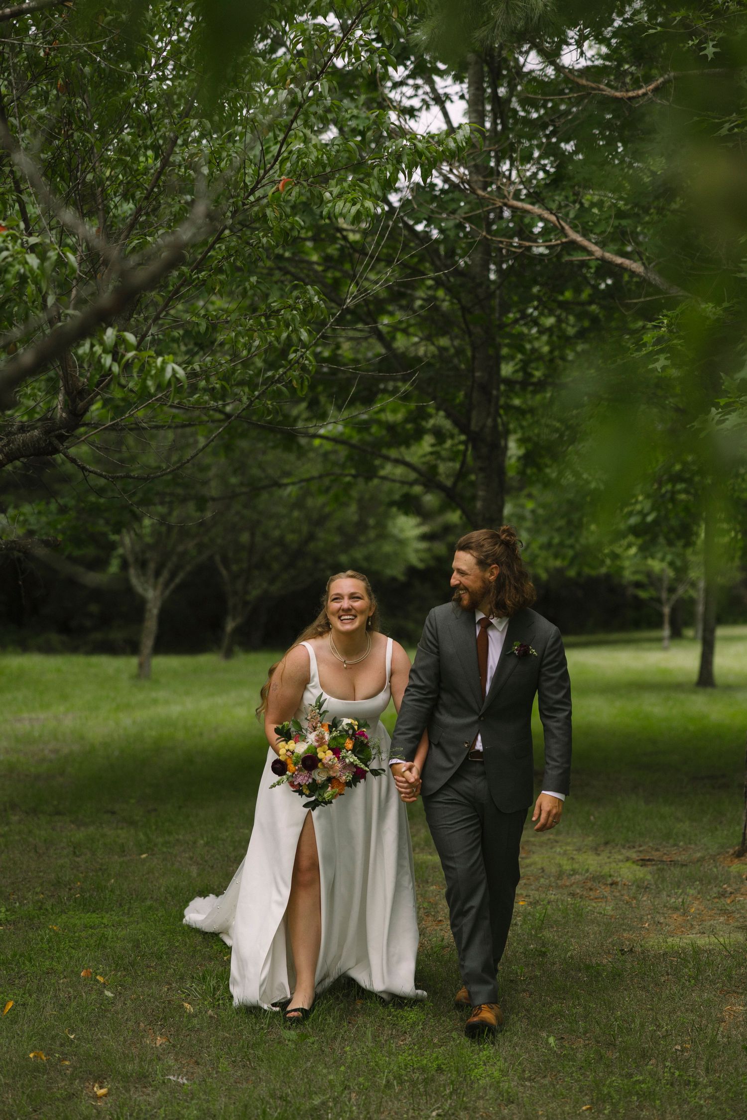 A wedding couple walks hand in hand through a serene garden path surrounded by lush trees.