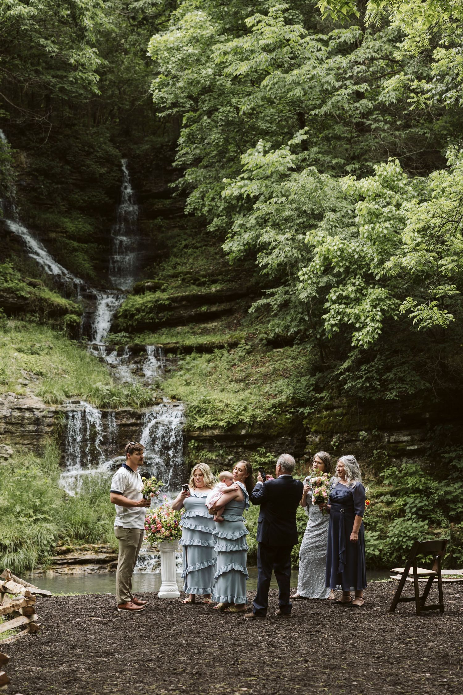 Wedding ceremony gathering in front of a cascading waterfall with guests and wedding party.