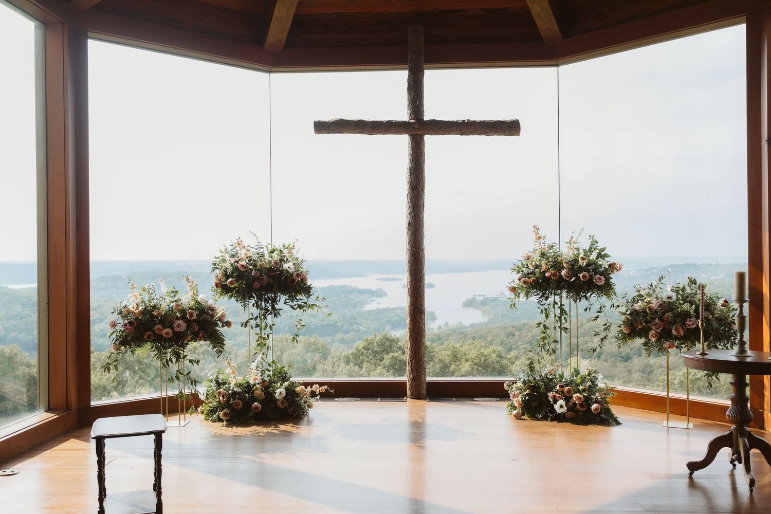 Wooden chapel altar with cross and hanging floral arrangements overlooking a scenic mountain view.