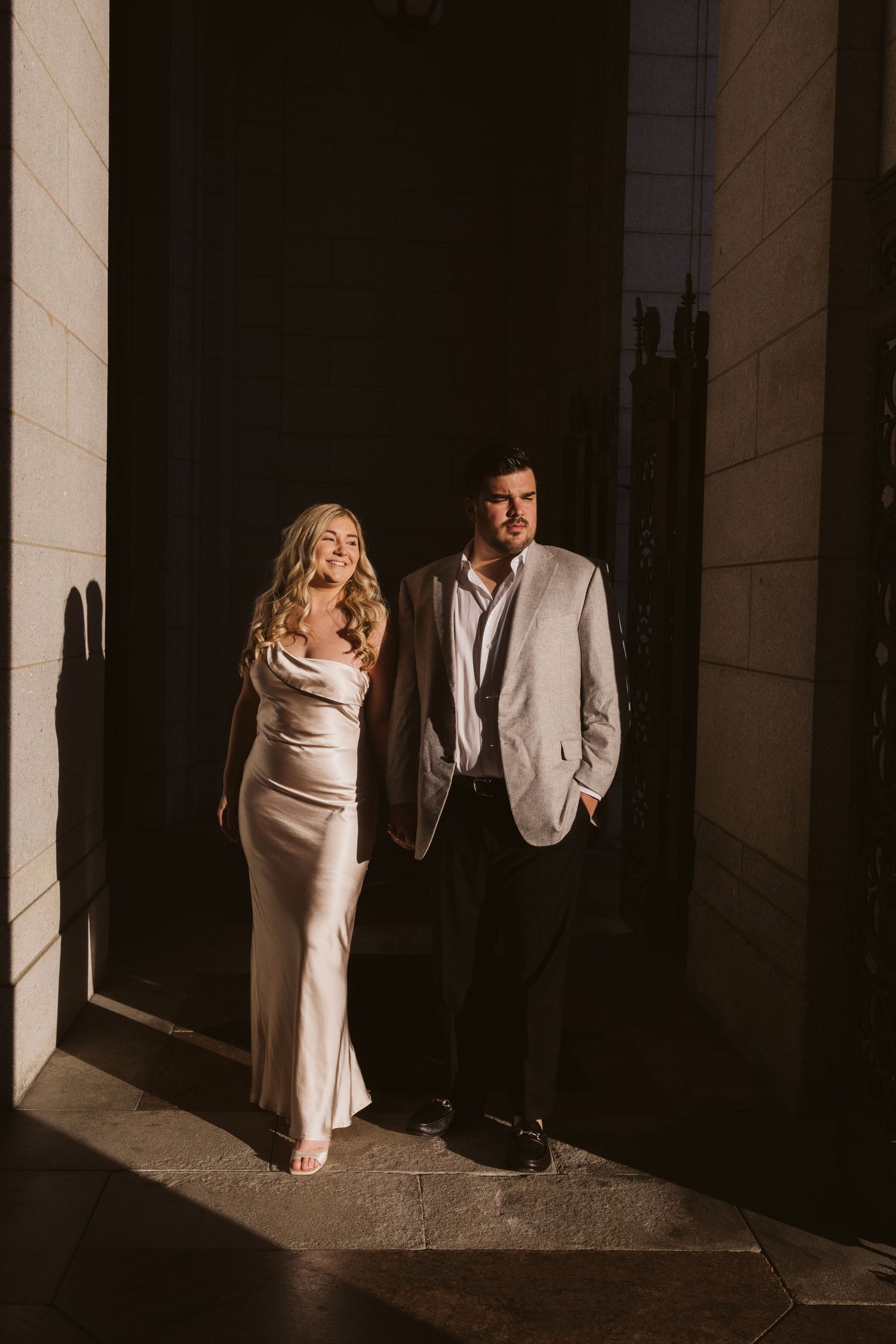 Stylish couple posing in dramatic lighting against stone columns.