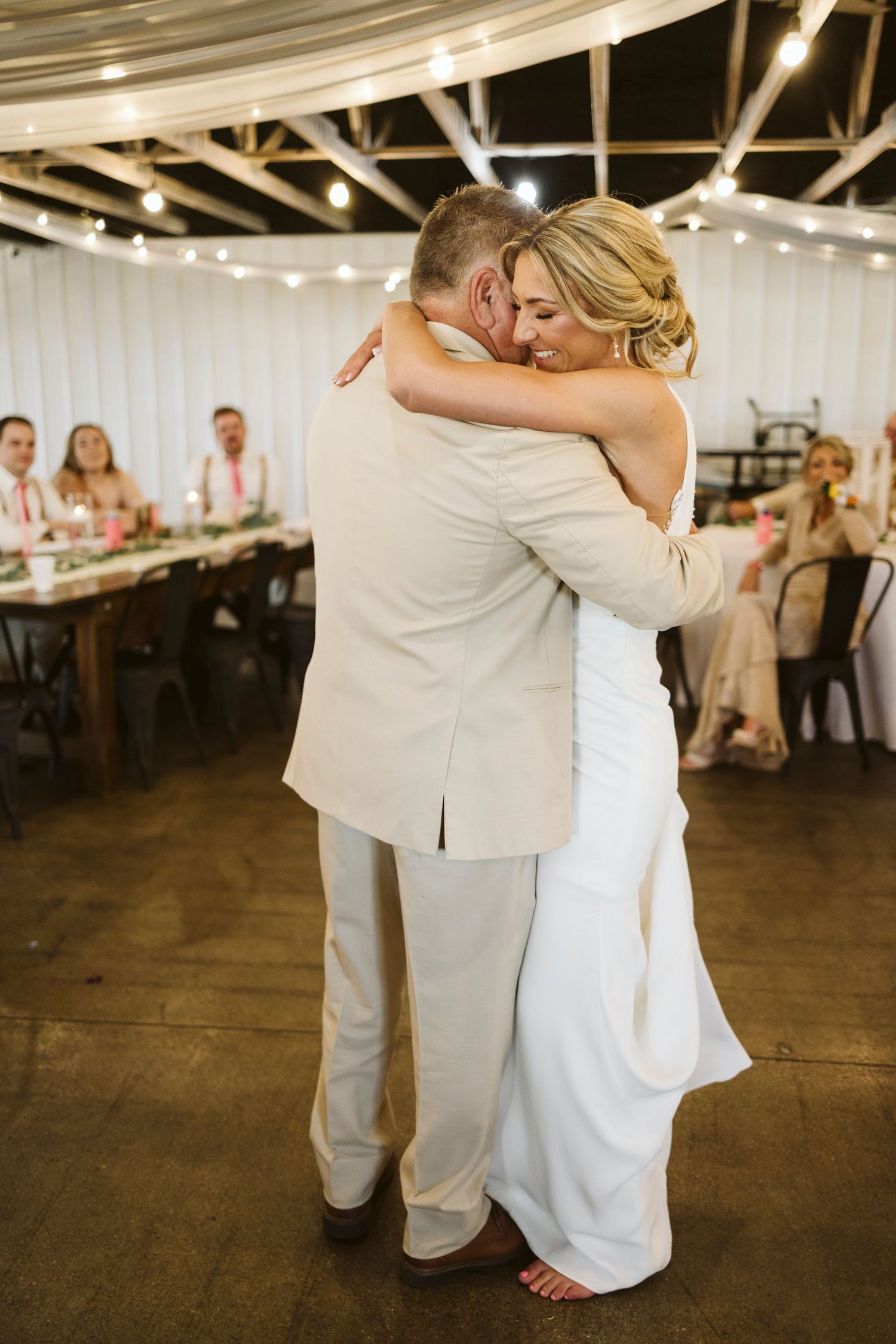 Couple shares intimate embrace during first dance at reception under string lights.