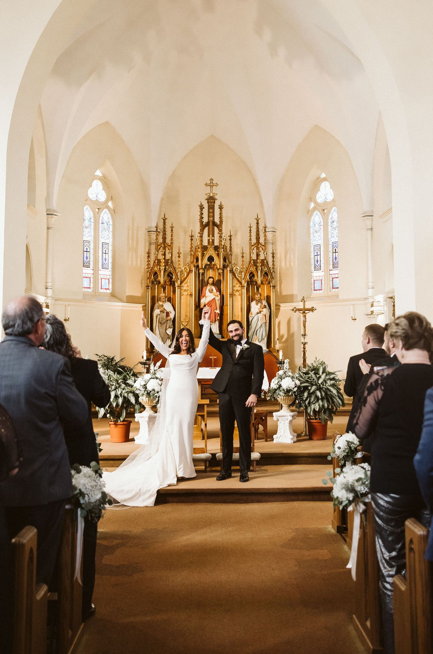 A bride and groom stand before an ornate golden altar during their church wedding ceremony.