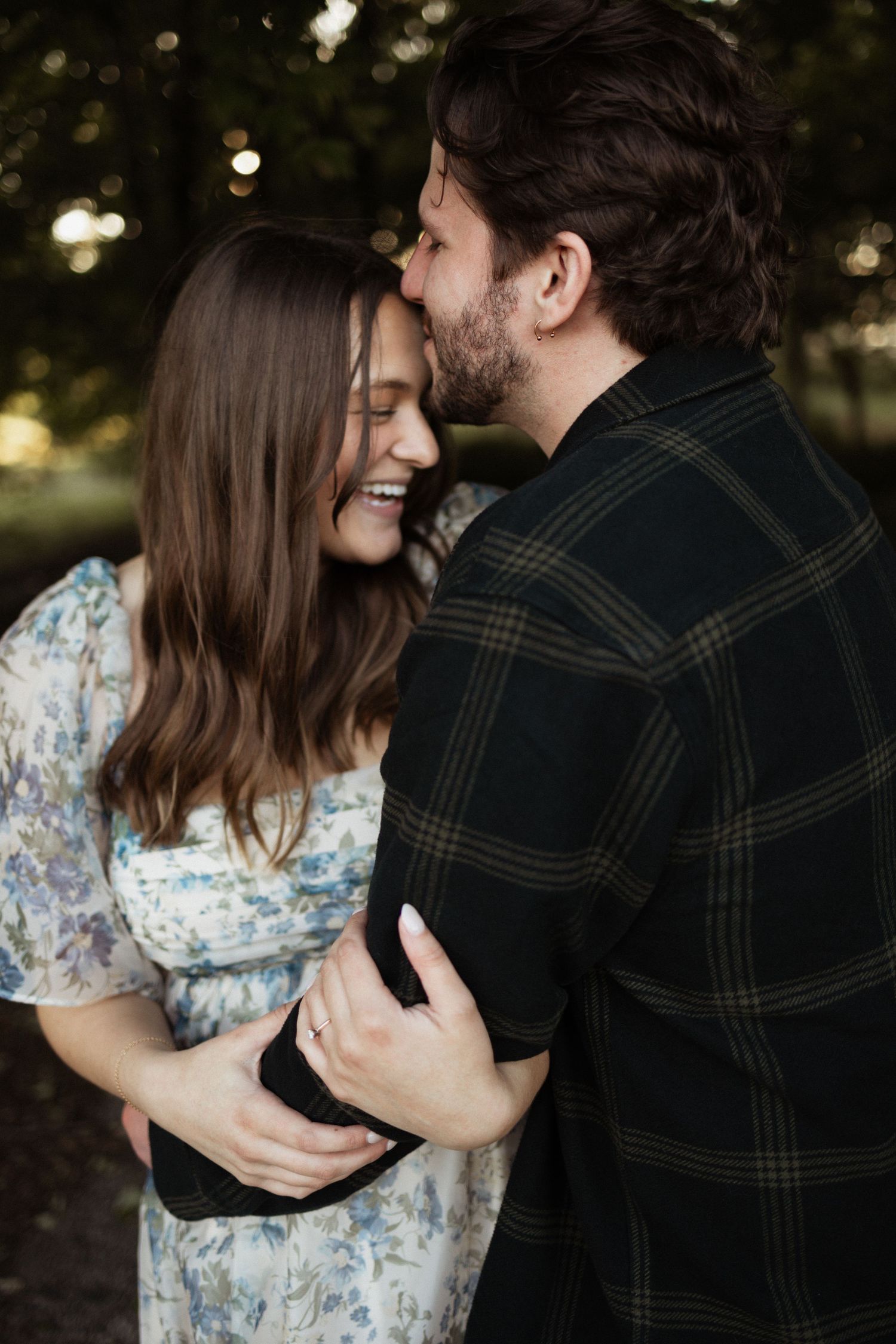 An intimate portrait of a couple embracing outdoors, with her in a floral dress and him in a plaid jacket.