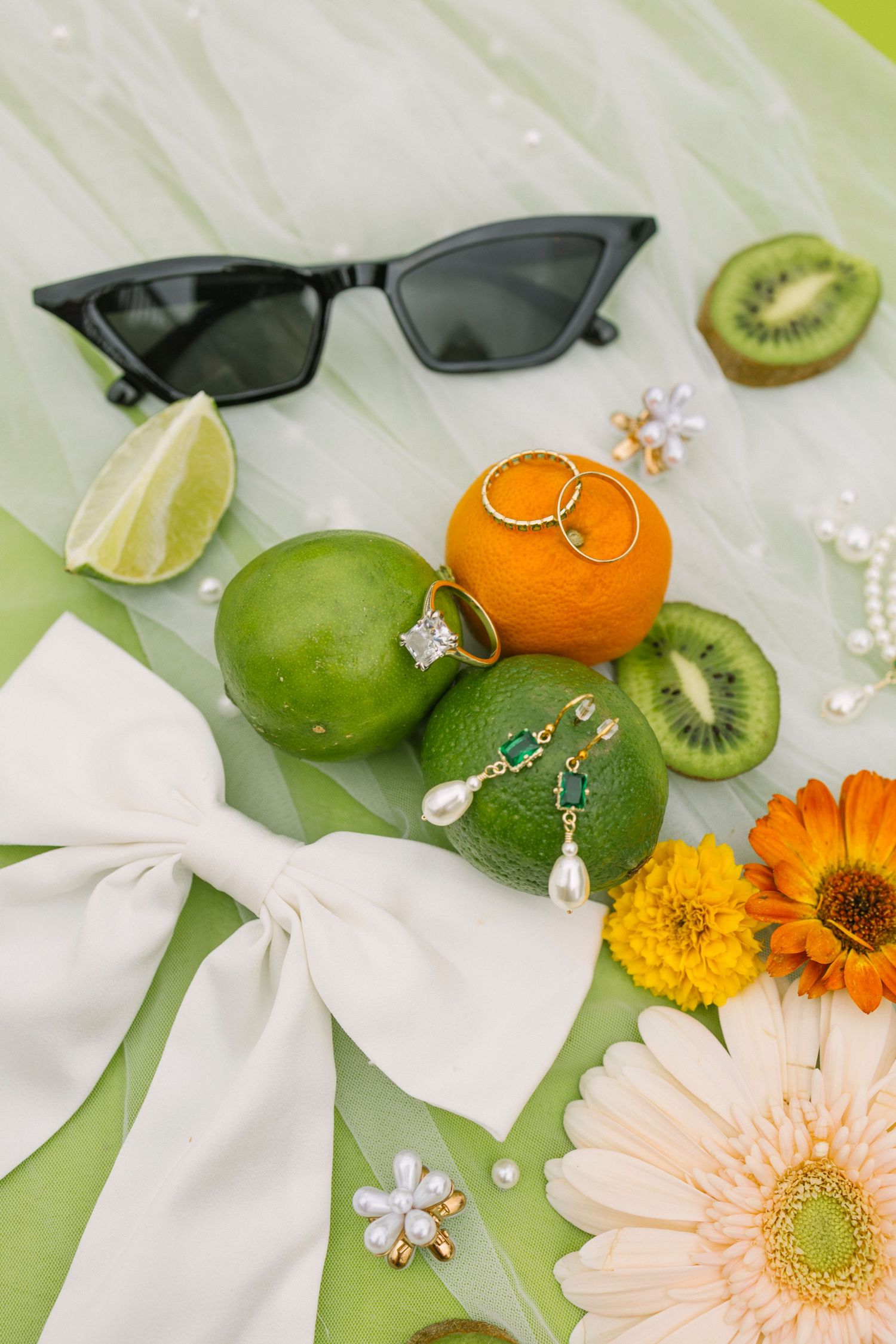 Wedding rings displayed on citrus fruits with sunglasses and flowers on a lime green background.