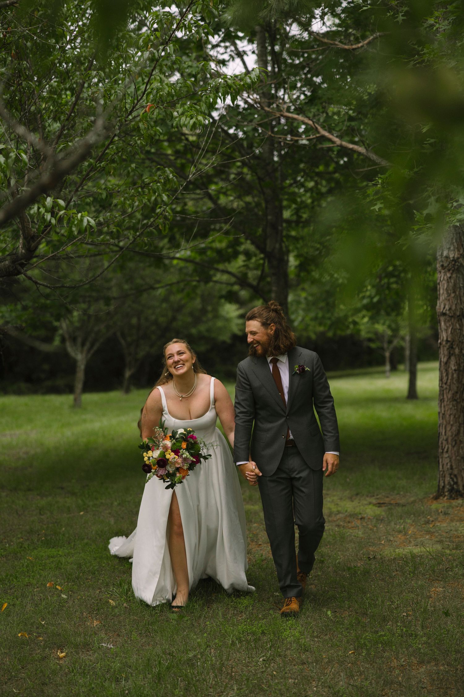 Newlyweds walk and laugh together in a green outdoor garden setting.