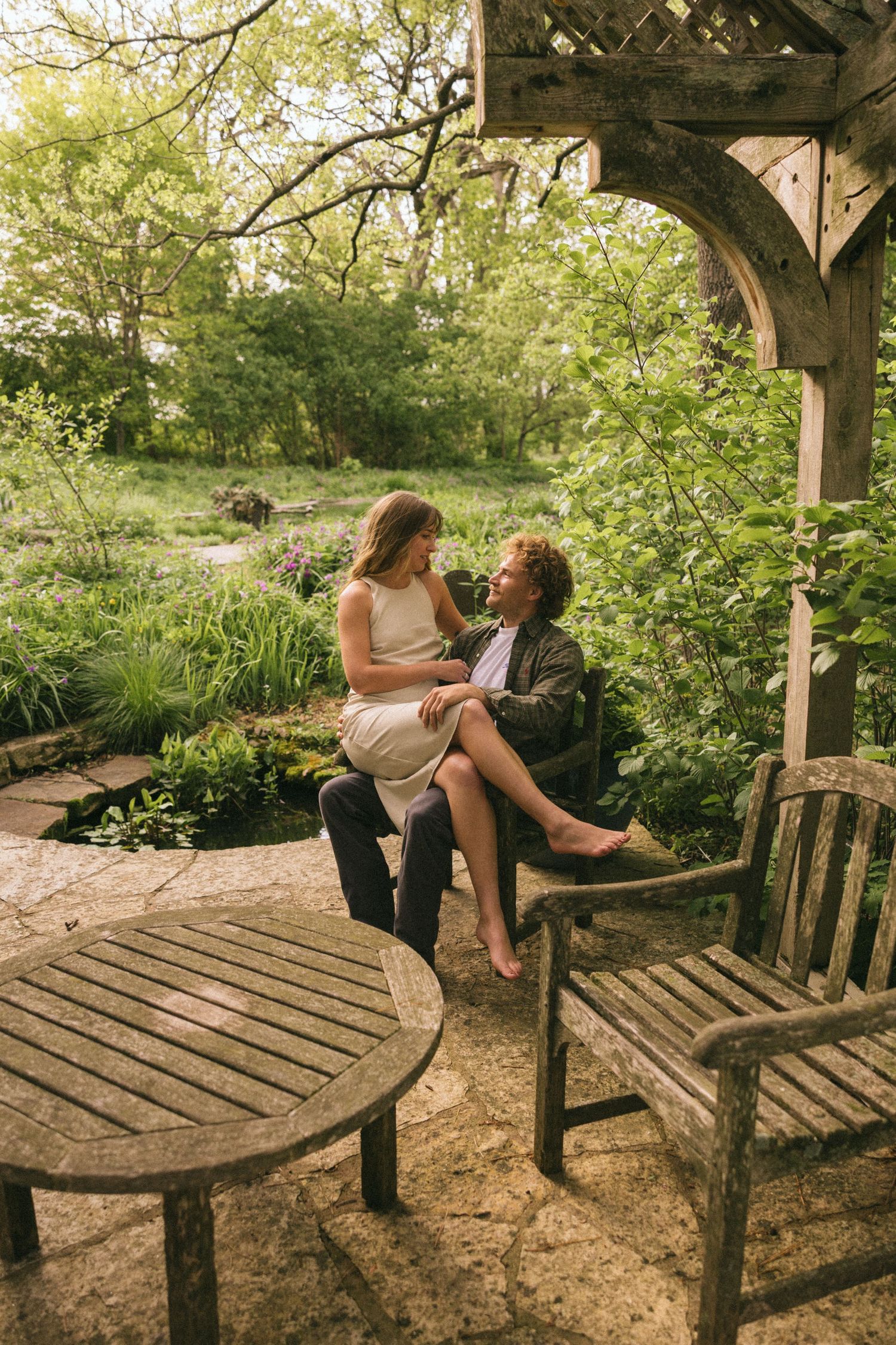 A couple shares a romantic moment on a wooden garden bench surrounded by lush greenery.