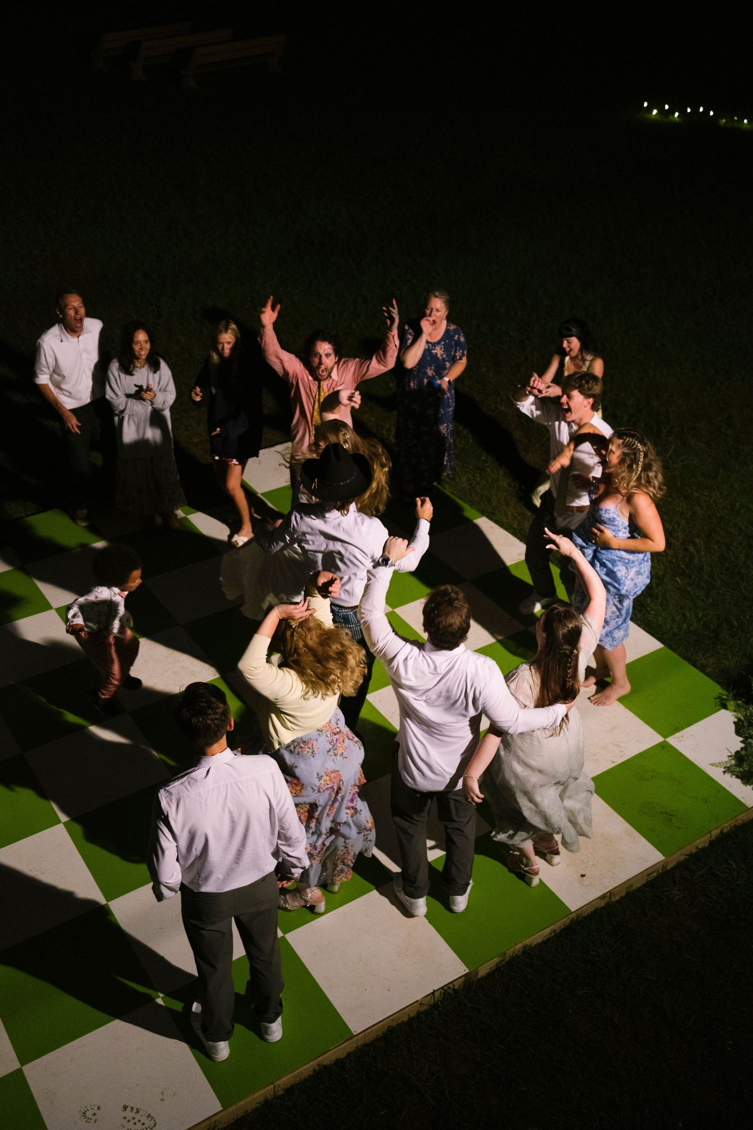 Guests dance together on a black and white checkered dance floor at an outdoor nighttime event.