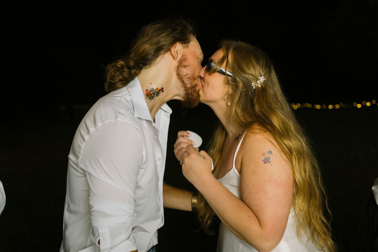 Couple in romantic embrace shares tender kiss in dark setting at celebratory outdoor event.