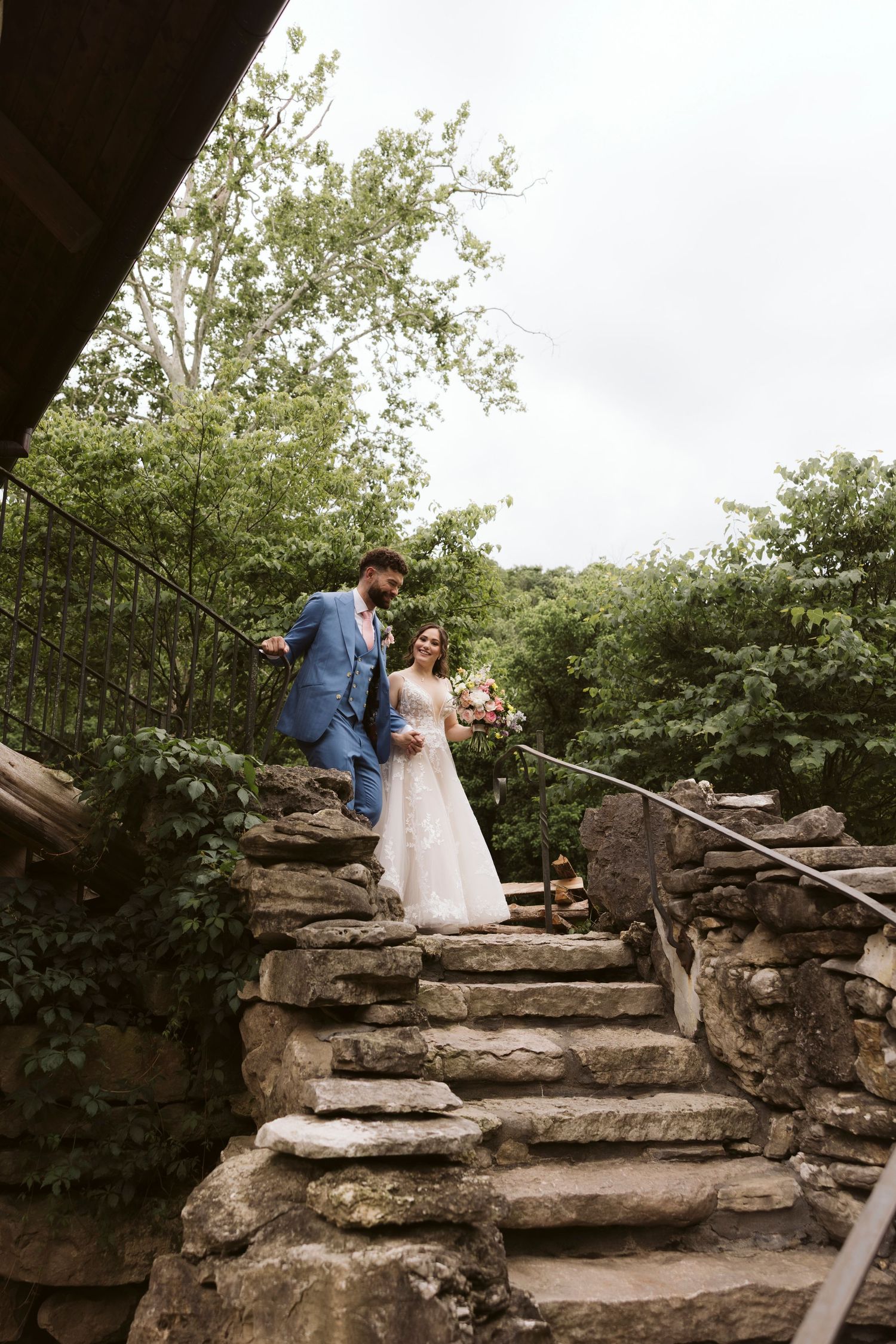Couple ascends rustic stone steps surrounded by lush greenery during their wedding photoshoot.
