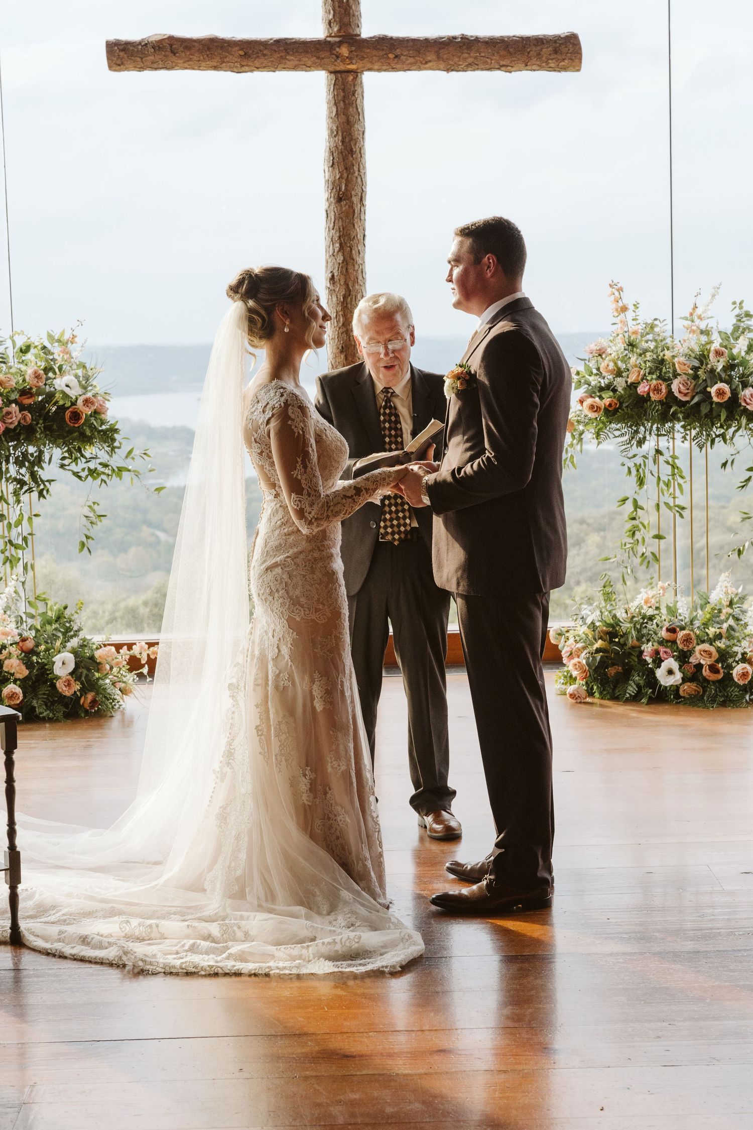 An intimate wedding ceremony under a wooden cross with floral arrangements and scenic hillside backdrop.