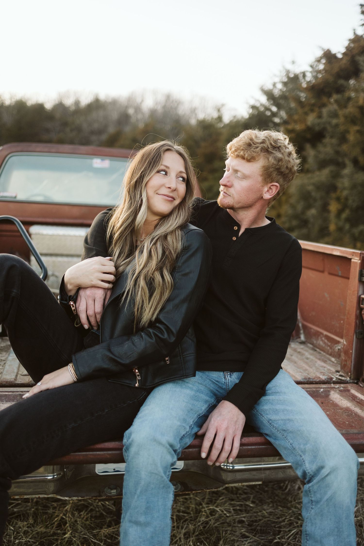 A couple sitting casually in a rustic truck bed during golden hour.
