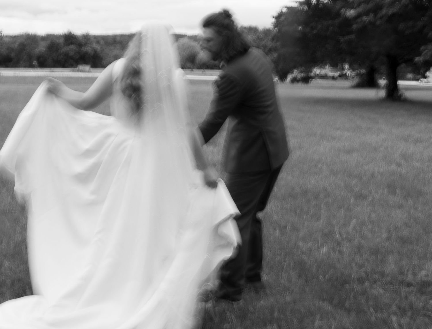 A photographer captures silhouetted figures in formal attire dancing together on a grassy field during an outdoor event.
