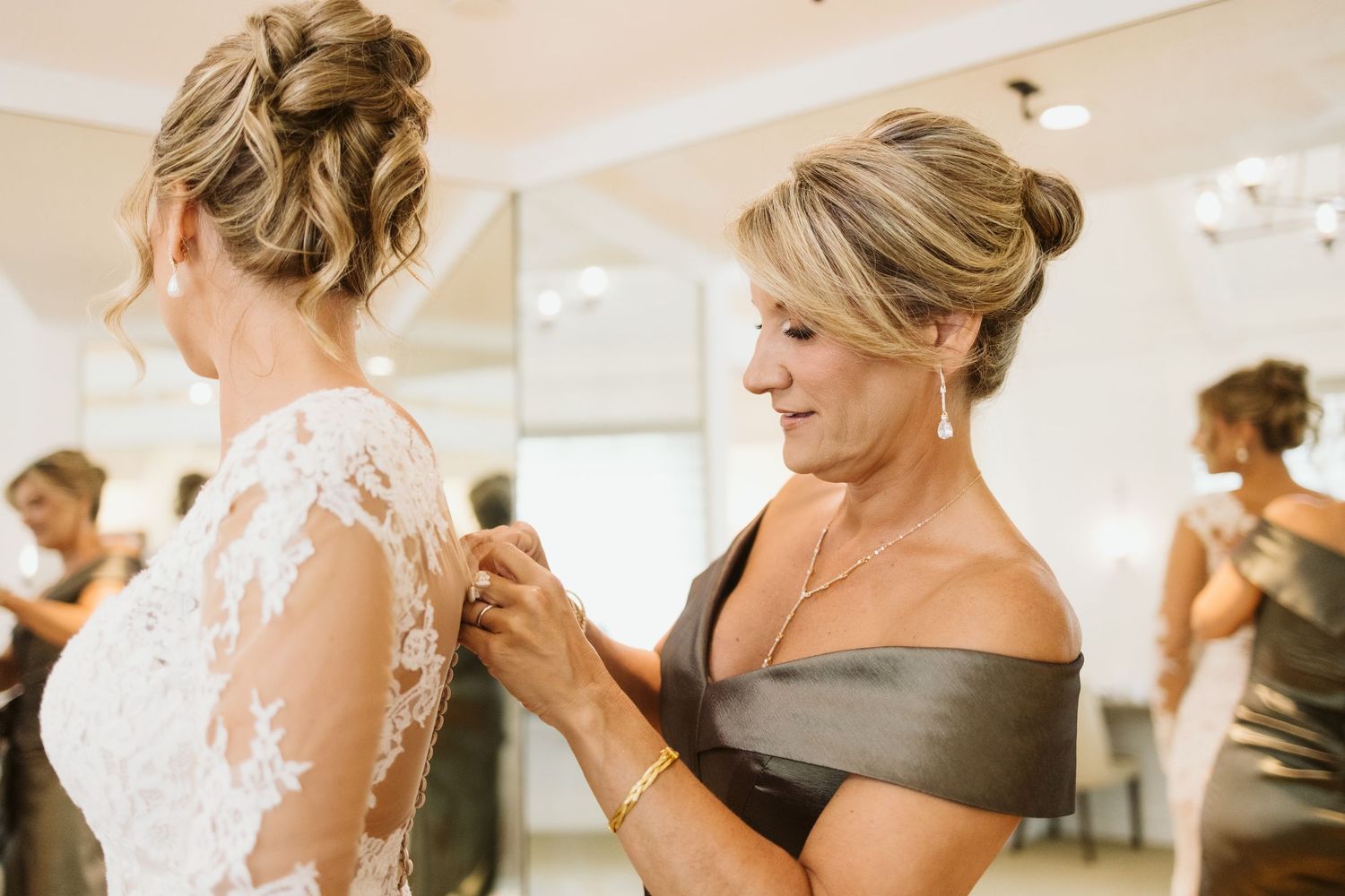 Bridesmaids help with final wedding dress preparations in a bright room.