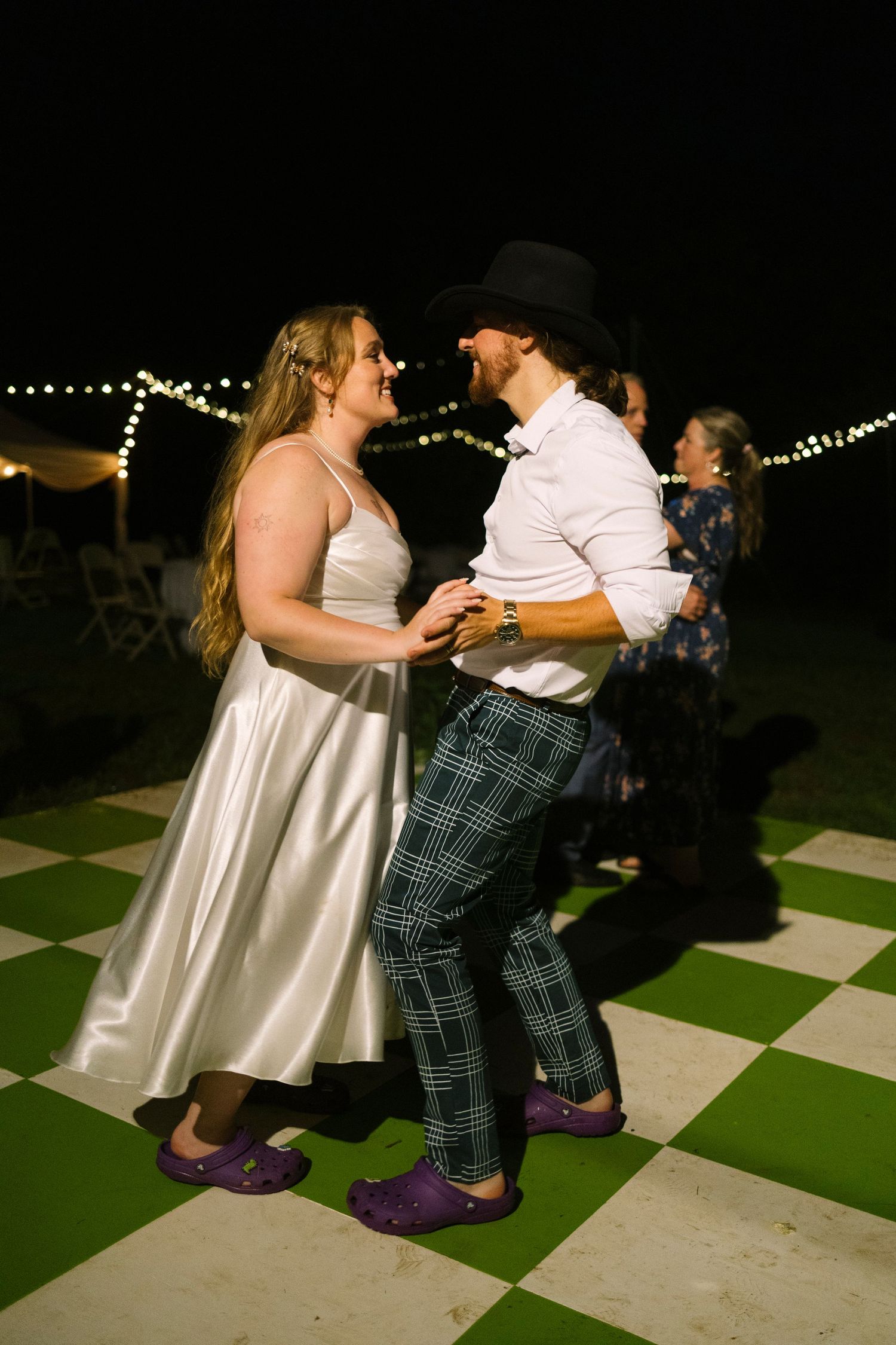 Two dancers in white and plaid outfits perform an energetic dance routine on a green and white checkered dance floor.