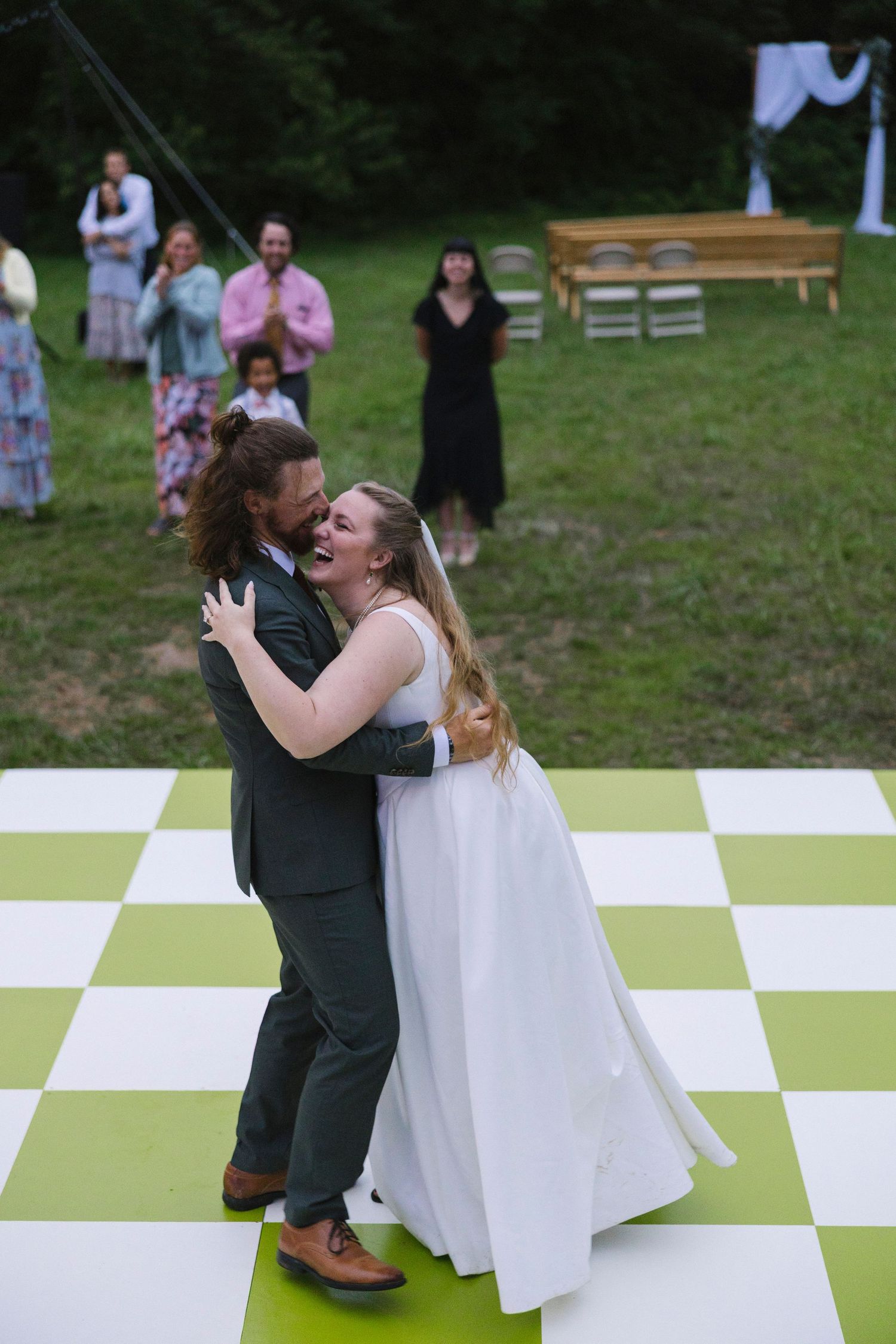 A couple shares a romantic outdoor dance during a special celebration on a green and white checkered dance floor.