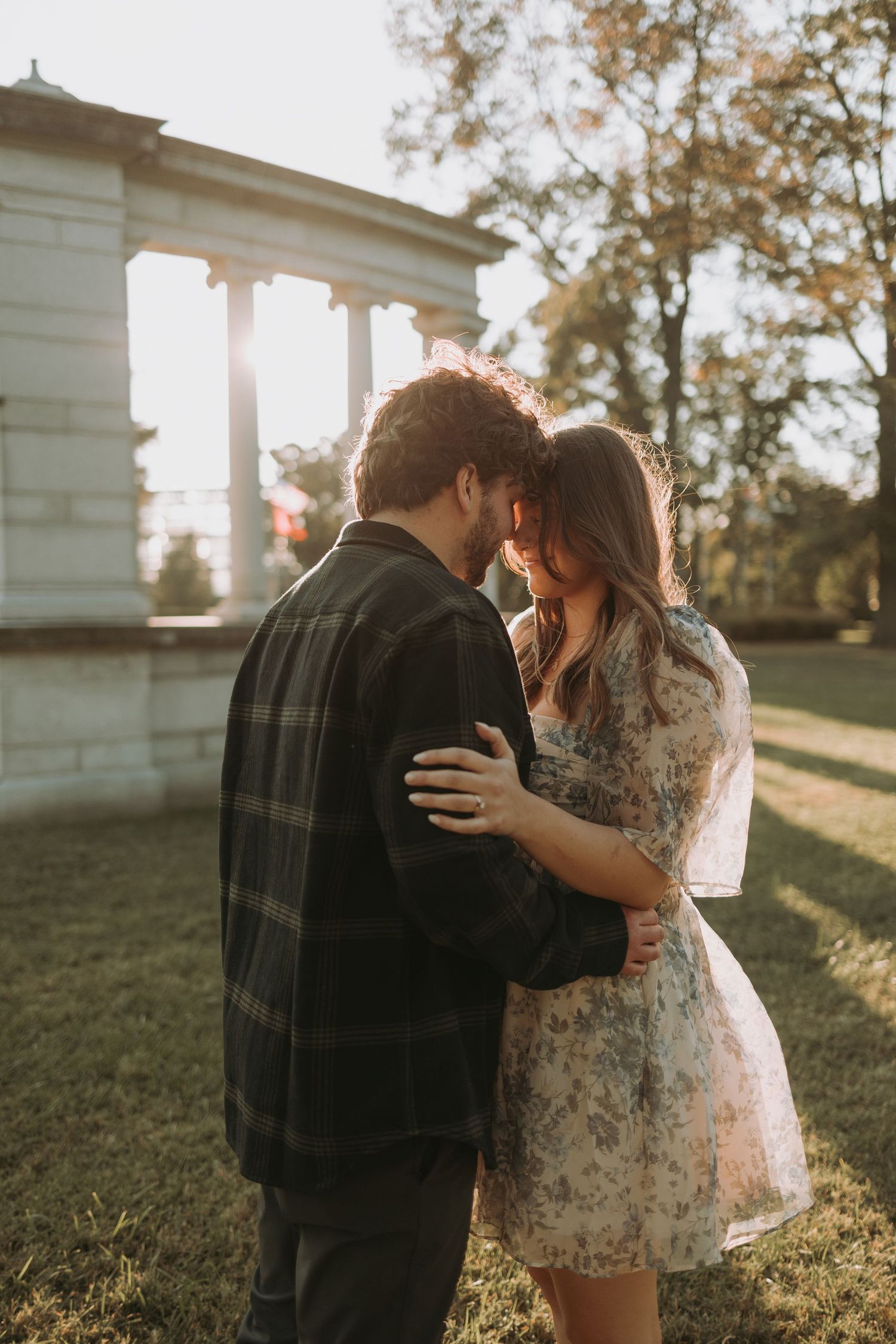 A sunset engagement photo of a couple embracing near a classical columned structure.