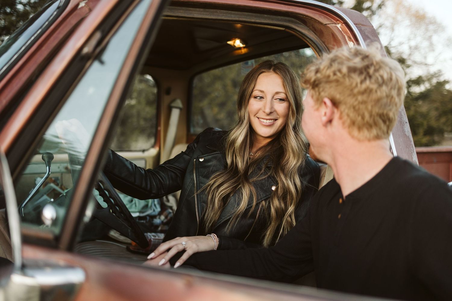 A couple sharing a moment inside a vintage red truck cabin.