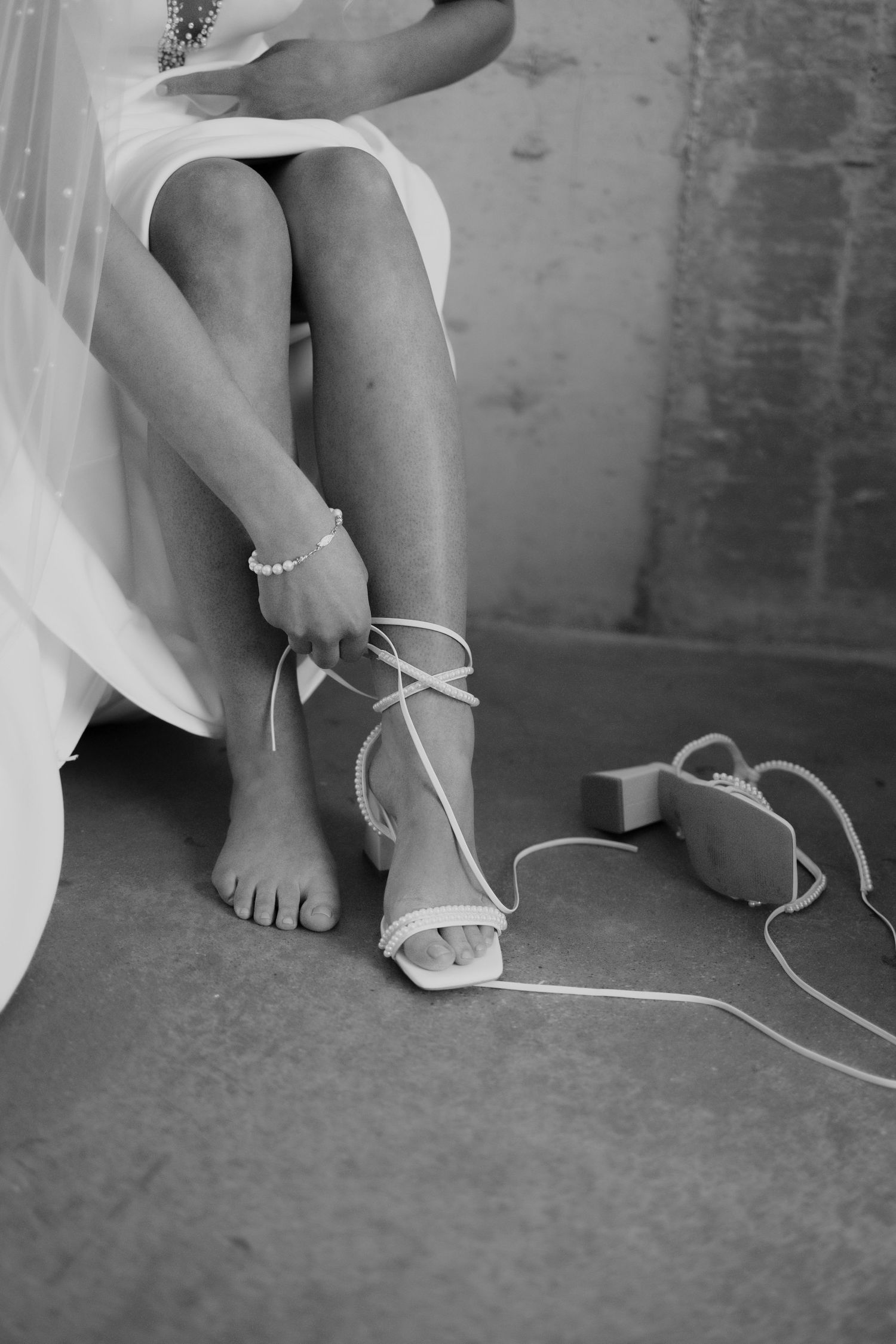 Black and white photo of someone fastening delicate white wedding sandals.