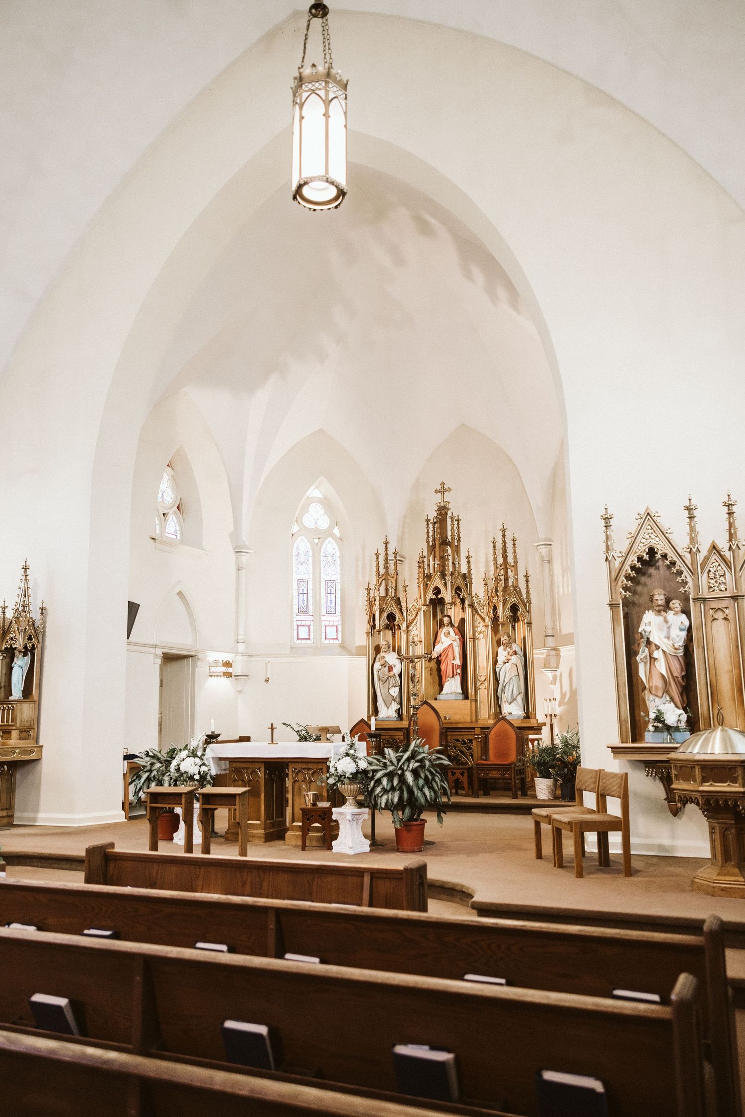 Interior view of a traditional Catholic church with Gothic architecture and wooden pews illuminated by pendant lights.
