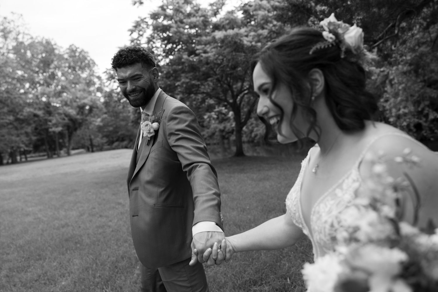 Wedding couple dances playfully in a grassy field during their outdoor celebration.