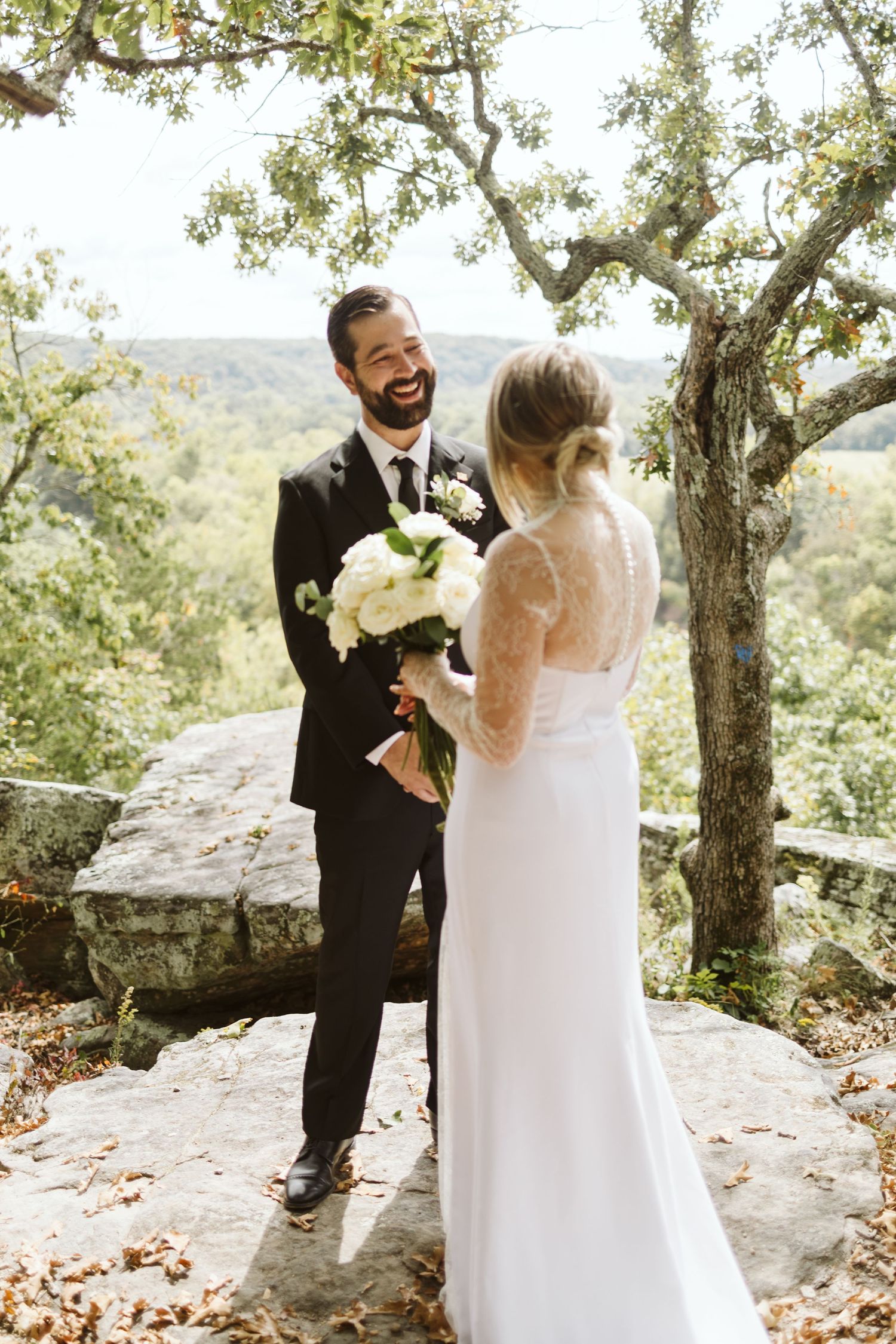 A joyful outdoor wedding moment captured among autumn trees on a rocky overlook.