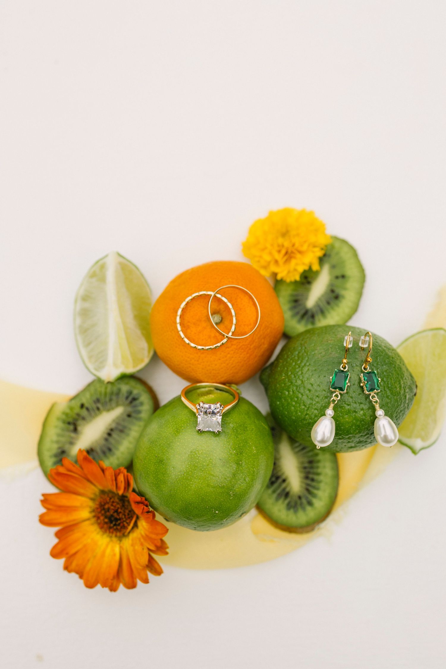 Colorful composition of fresh sliced oranges, kiwis, limes and orange marigold flowers with silver jewelry on white background.
