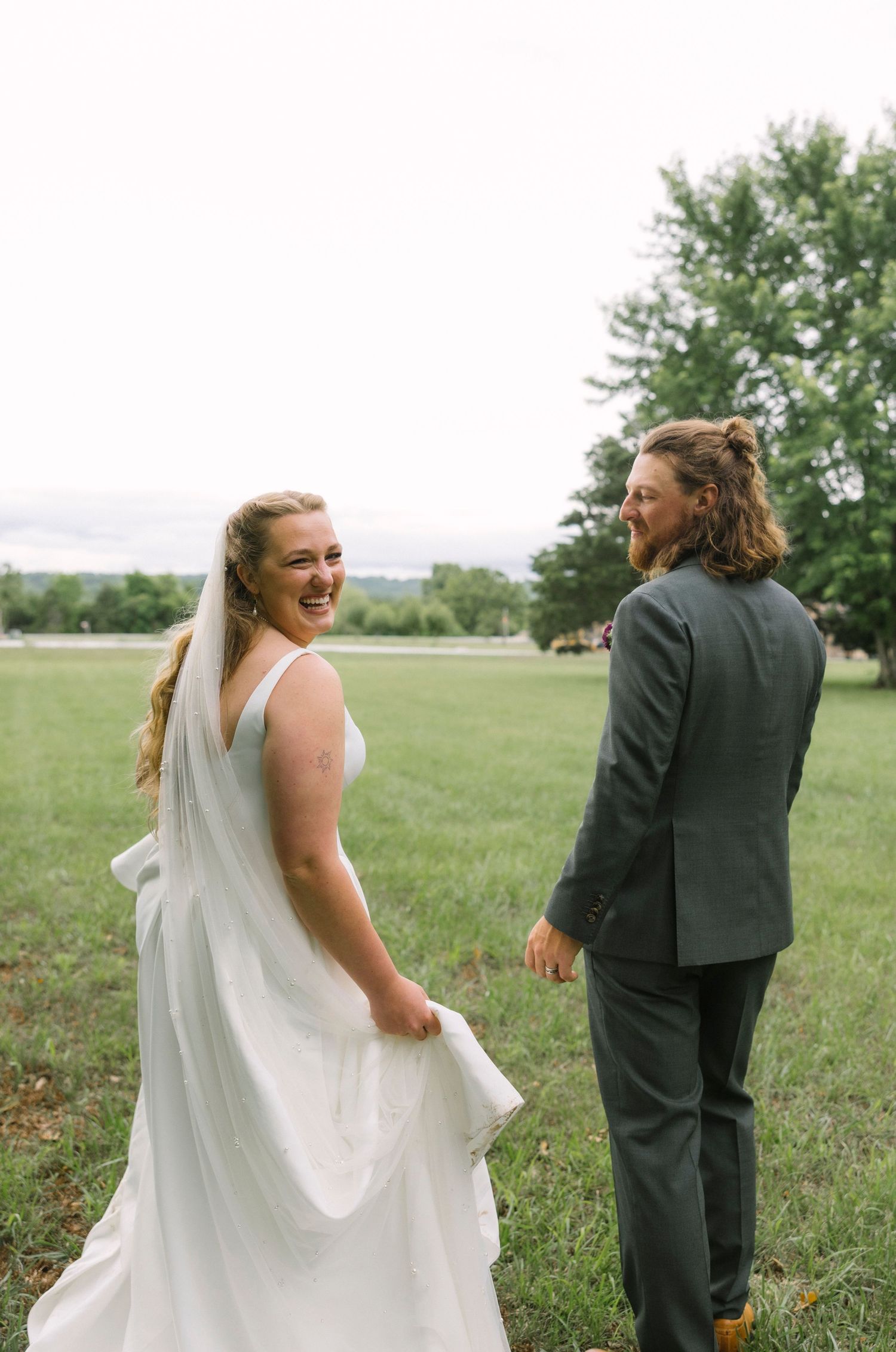 A joyful couple shares a candid moment together in a grassy field during their wedding day.