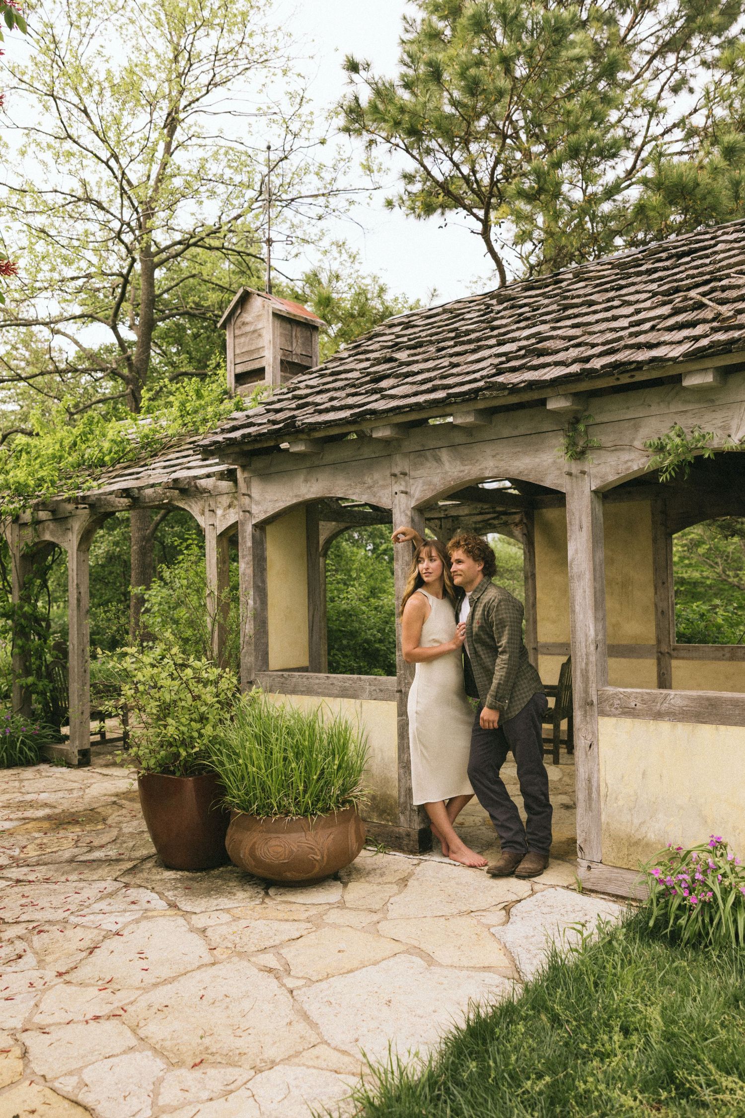 A couple embracing under an architectural pergola with stone flooring and garden landscaping.