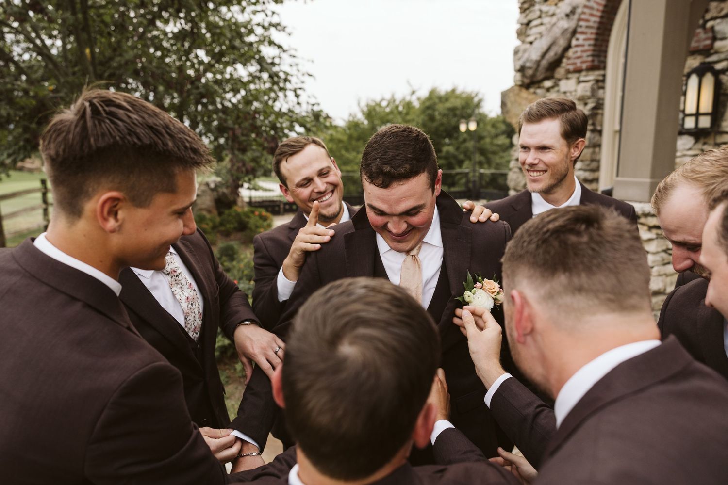 Groomsmen in dark suits sharing a joyful moment outside during wedding celebrations.