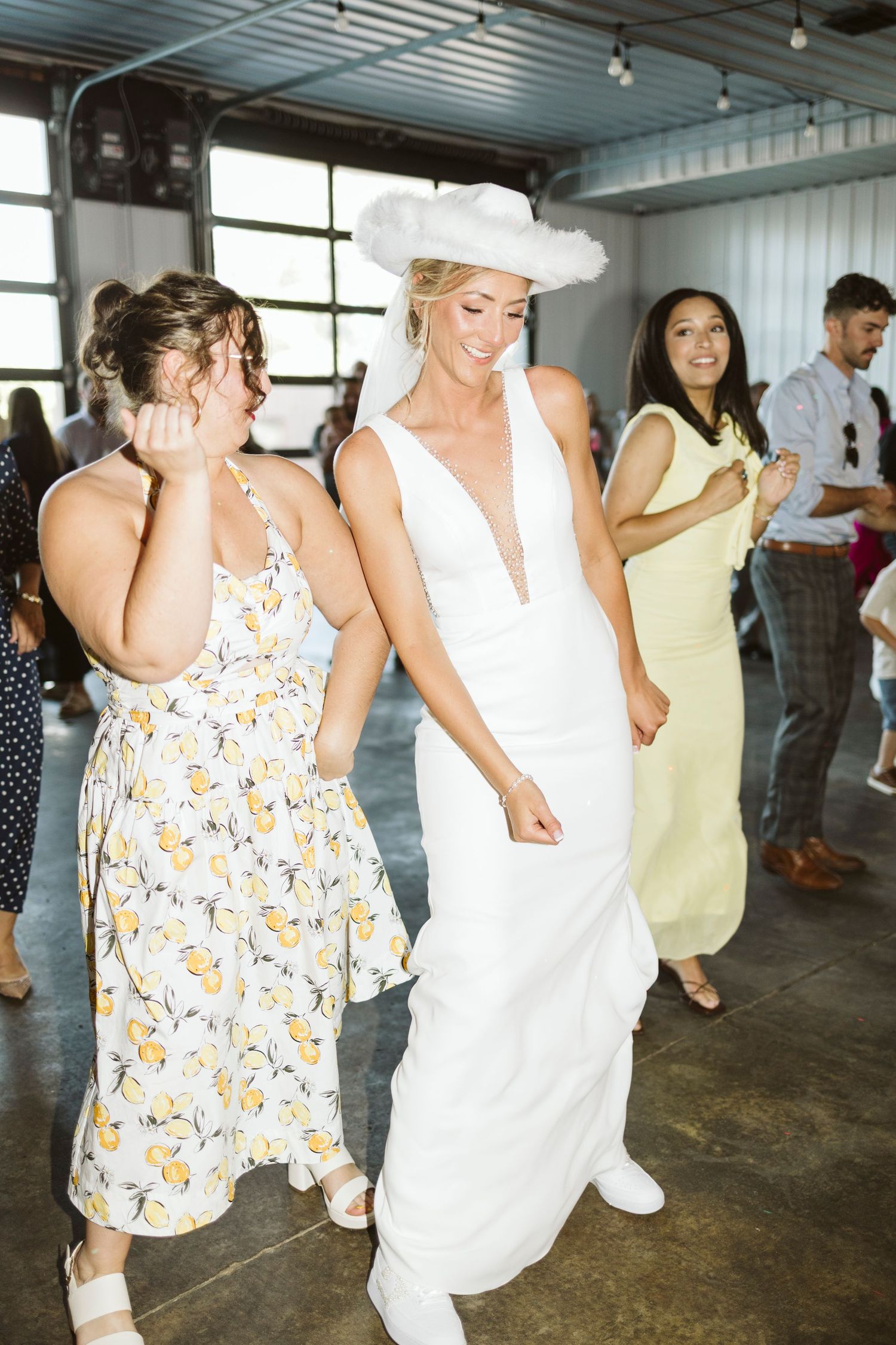Wedding guests dancing and celebrating in a rustic indoor venue with industrial ceiling.