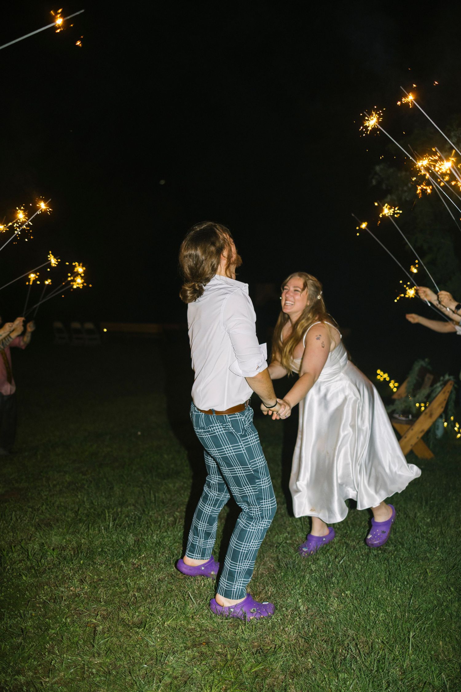 People dancing at an outdoor party at night with sparklers creating bright trails of light in the dark.