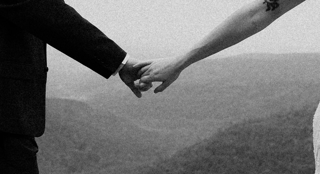 Two hands reach out and hold each other against a blurry black and white horizon background.